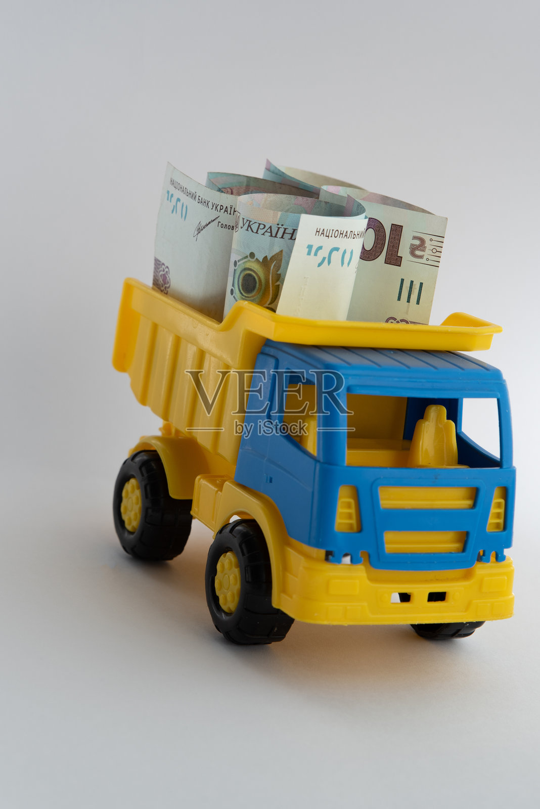 现金、钱，一辆黄色和蓝色的玩具车在白色背景上载着乌克兰格里夫纳纸币。照片摄影图片