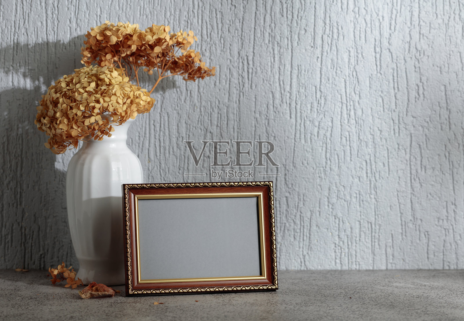 空的相框和白色花瓶，里面插着干花，背景是灰色墙壁。照片摄影图片