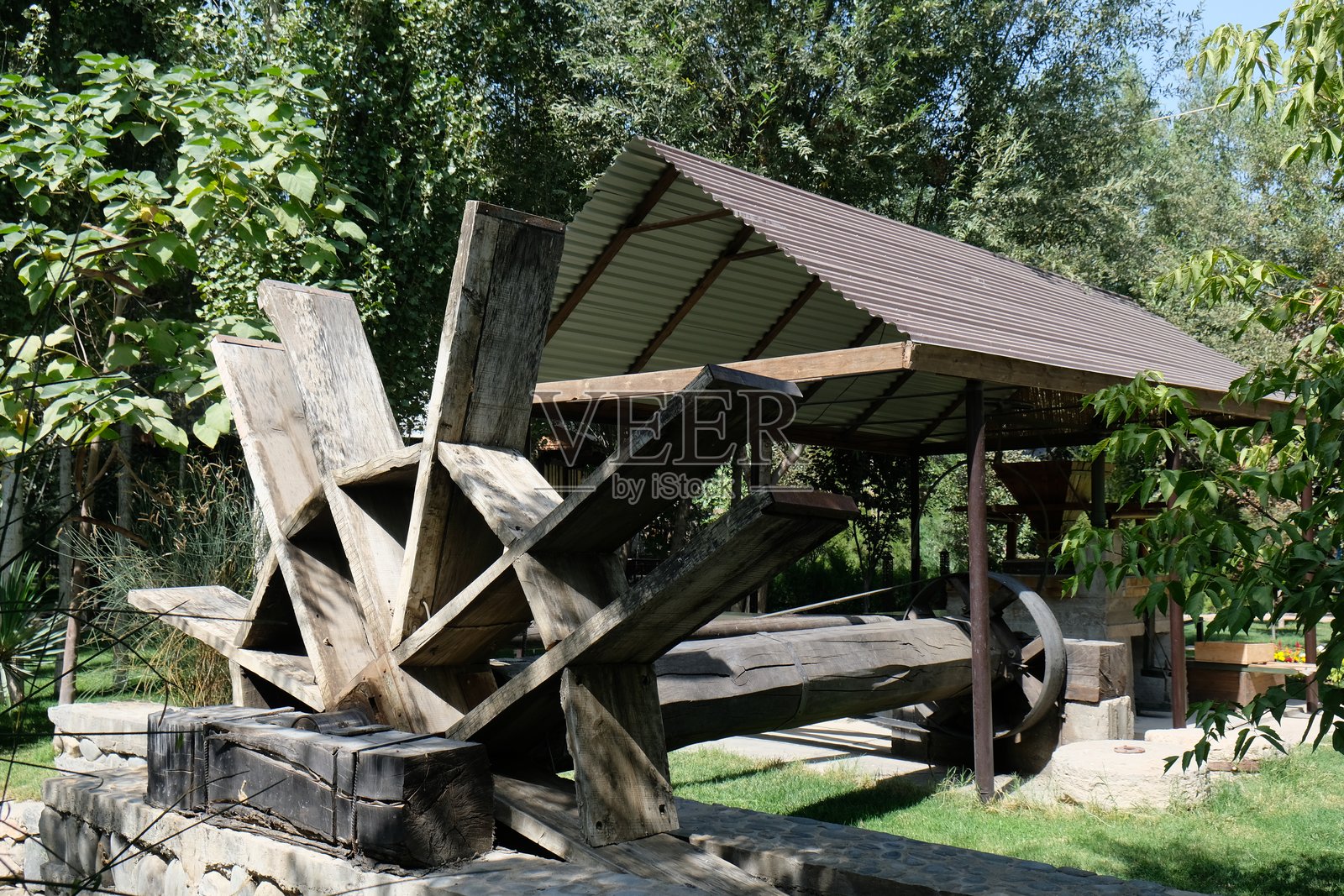 位于郁郁葱葱公园中的水车机制，展示了传统工程与自然和谐的结合，背景为白天的景象。照片摄影图片