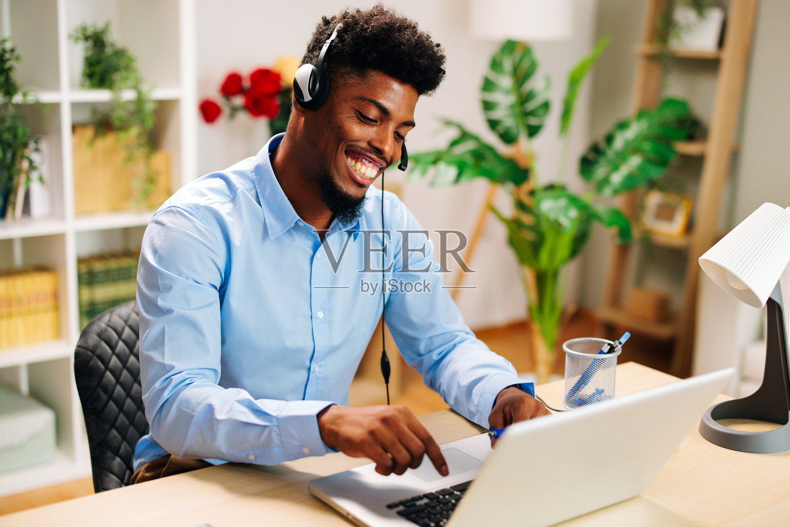 快乐的年轻人在家中使用笔记本电脑和耳机远程工作照片摄影图片