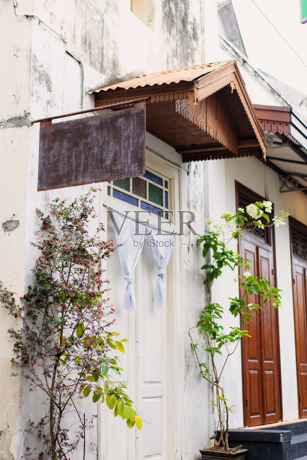 印尼索罗殖民时代建筑上的乡村空白铁牌，配有木门和盛开的植物照片摄影图片