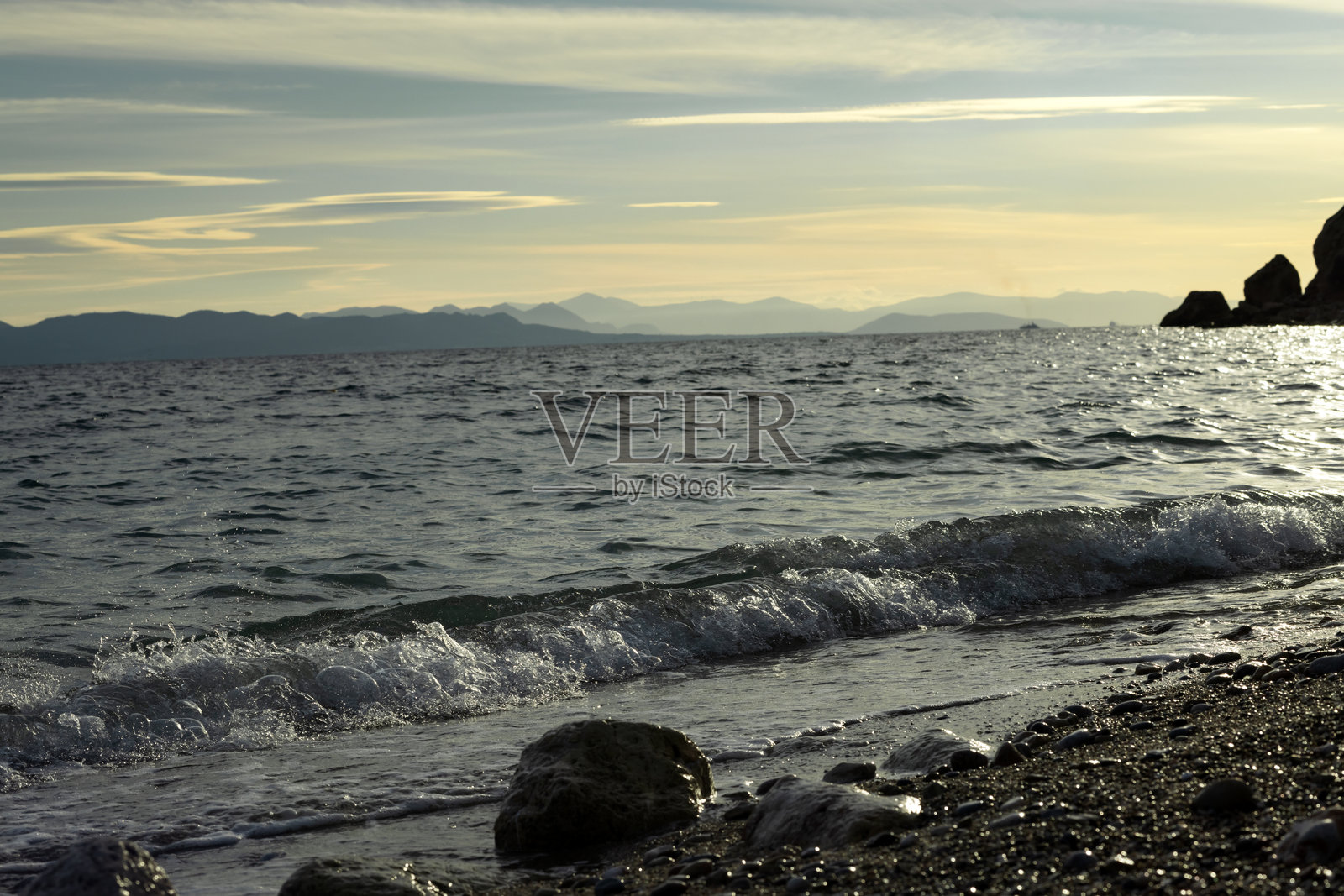 海滩上波浪拍打卵石，圆润的巨石轮廓在岬角上。照片摄影图片