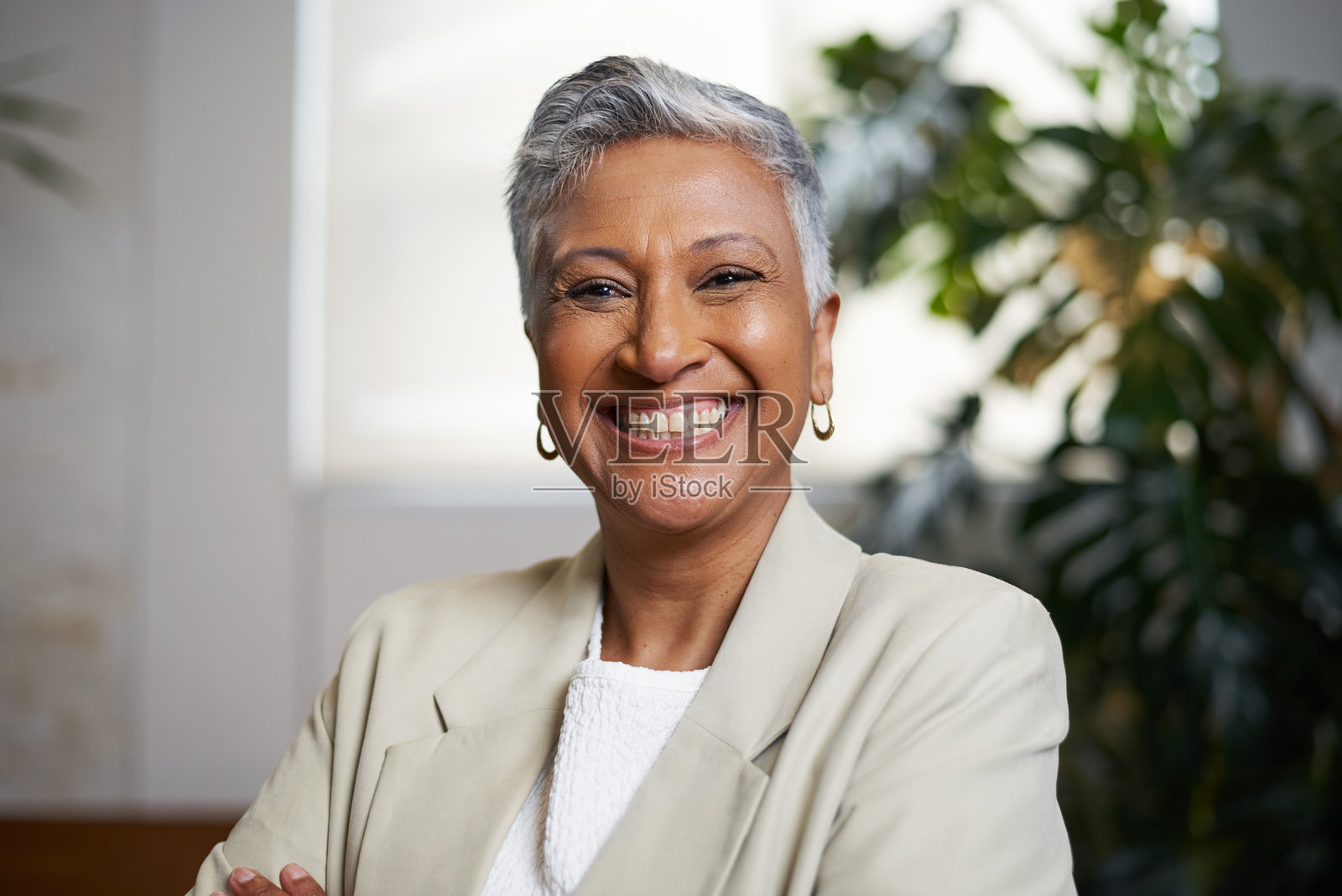 自信的成熟的女性在现代室内环境中微笑，周围环绕着绿色植物照片摄影图片