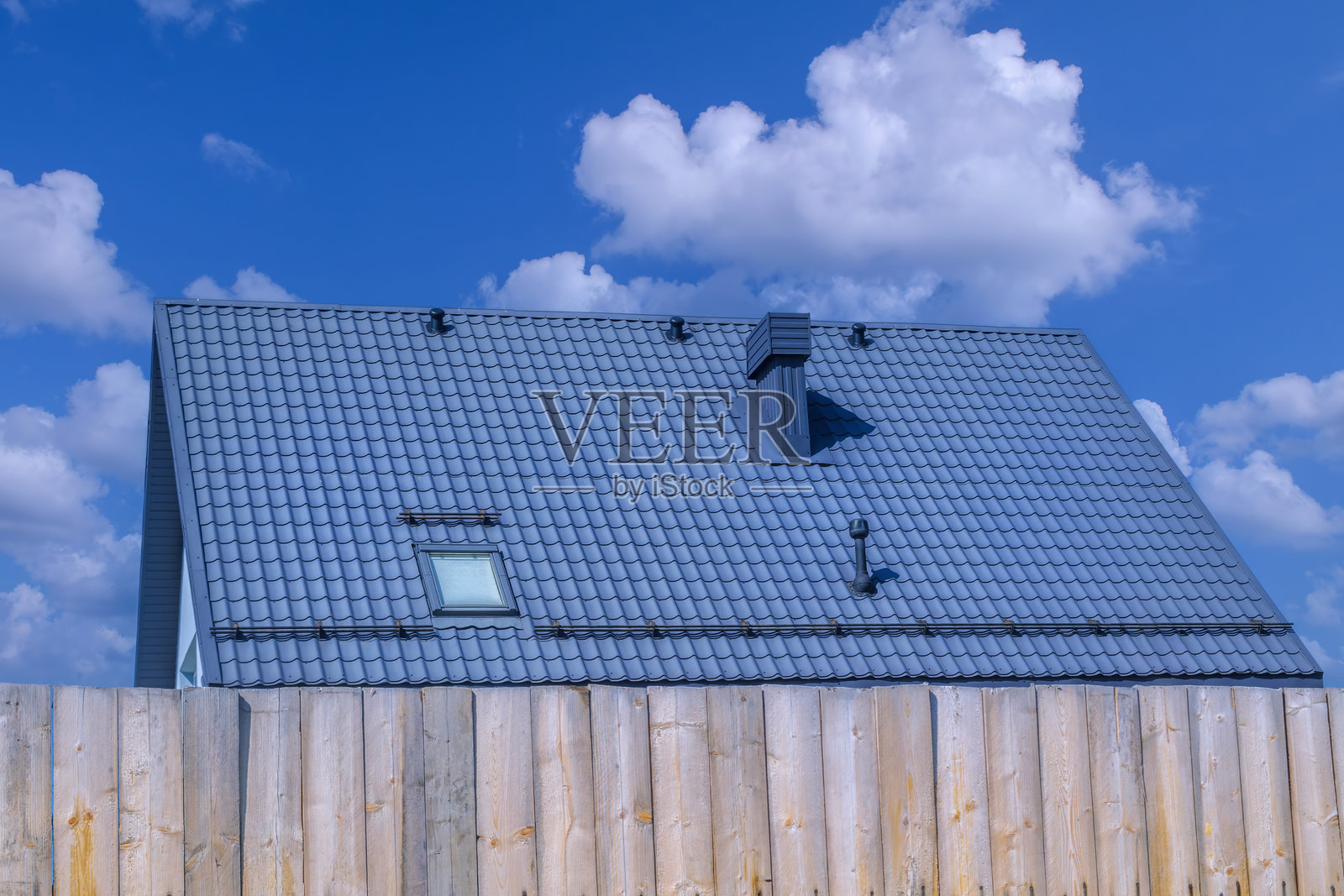 现代房屋前景中的乡村木栅栏，屋顶为石板材质，映衬在明亮的蓝天之下。照片摄影图片