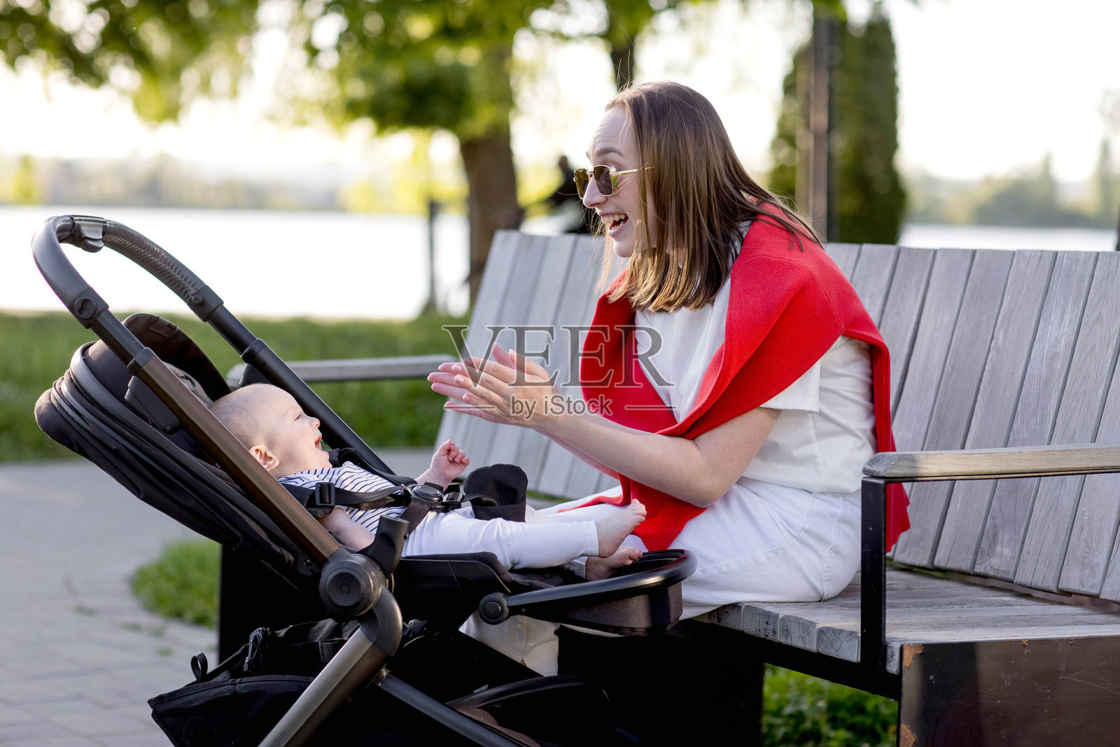 年轻母亲和她可爱的宝宝坐在公园长椅上照片摄影图片