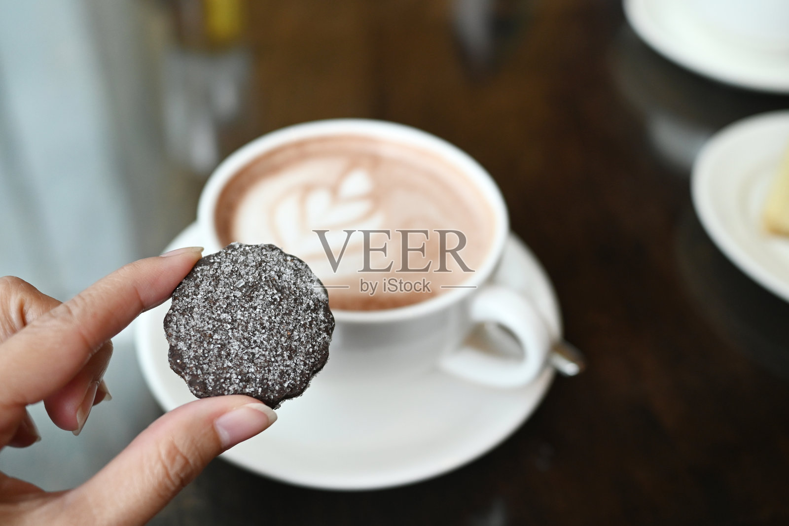 手握巧克力曲奇饼干，旁边是一杯咖啡的特写镜头照片摄影图片