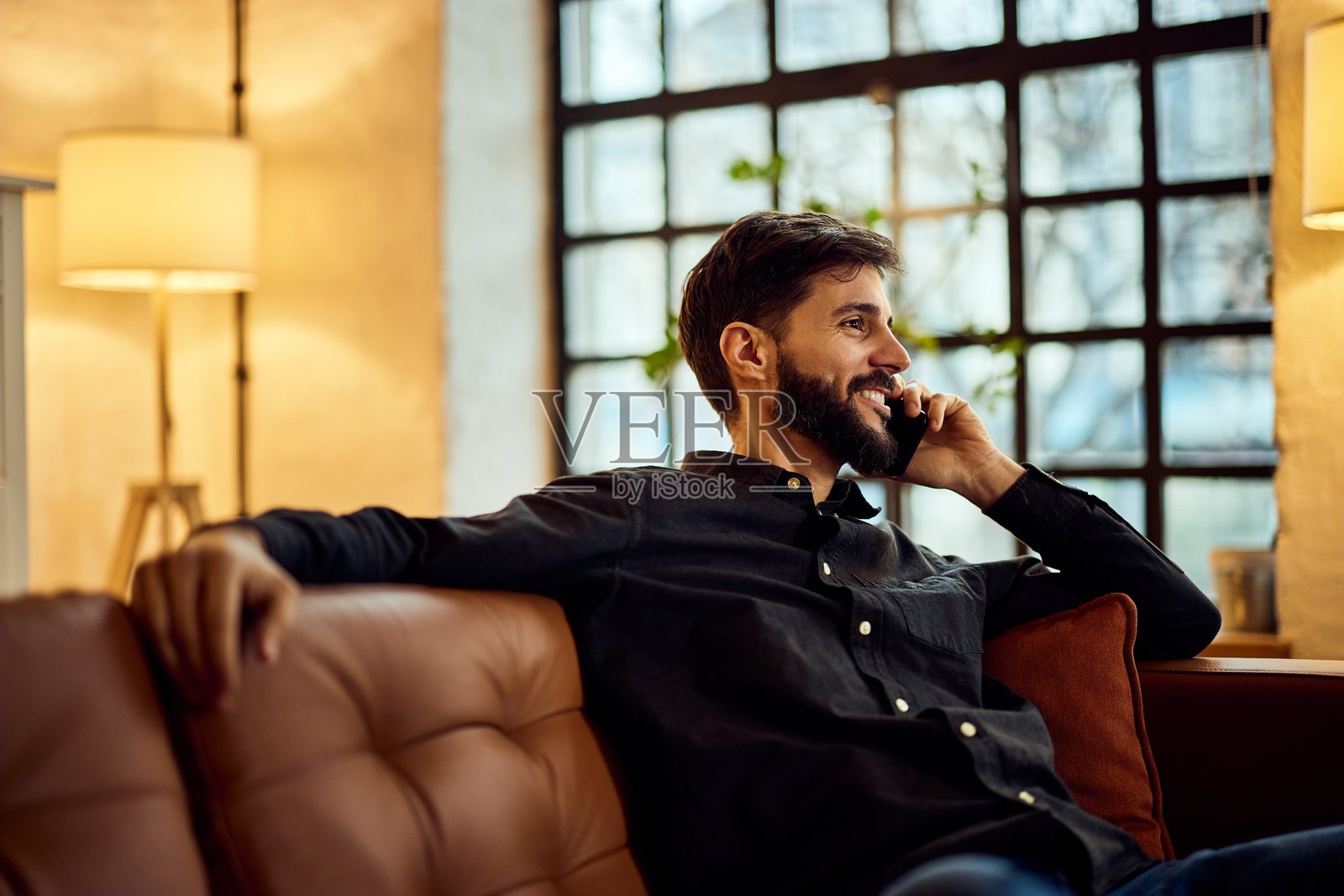 男人在舒适的客厅里微笑着放松，使用智能手机交谈。照片摄影图片