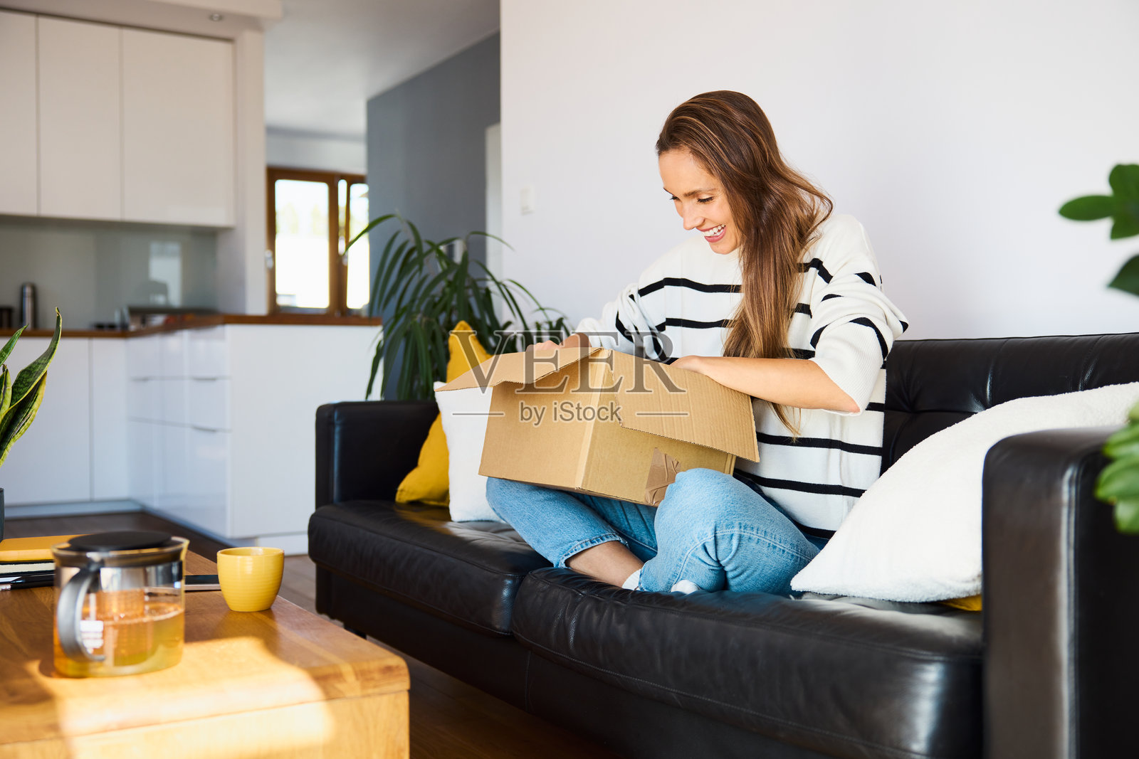 兴奋的女性顾客坐在公寓沙发上打开快递包裹照片摄影图片