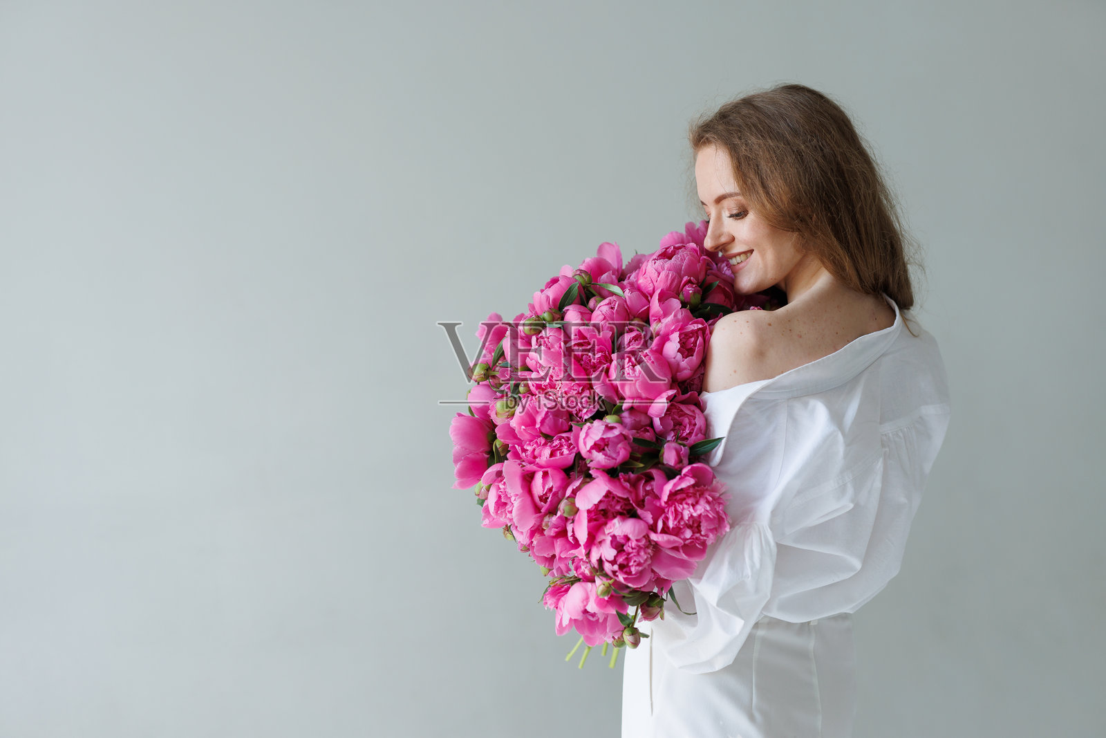 身穿白色服装的时尚女性，头上覆盖着粉色牡丹，摆姿势于简约背景前，展现艺术花卉时尚概念。照片摄影图片