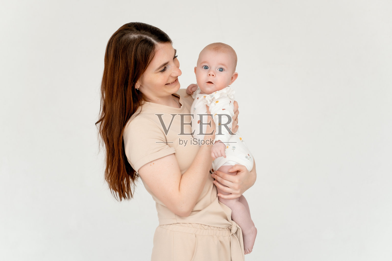 年轻母亲在白色背景和床上抱着她的小女儿，温柔地表达母爱与关怀，留有文字空间。照片摄影图片