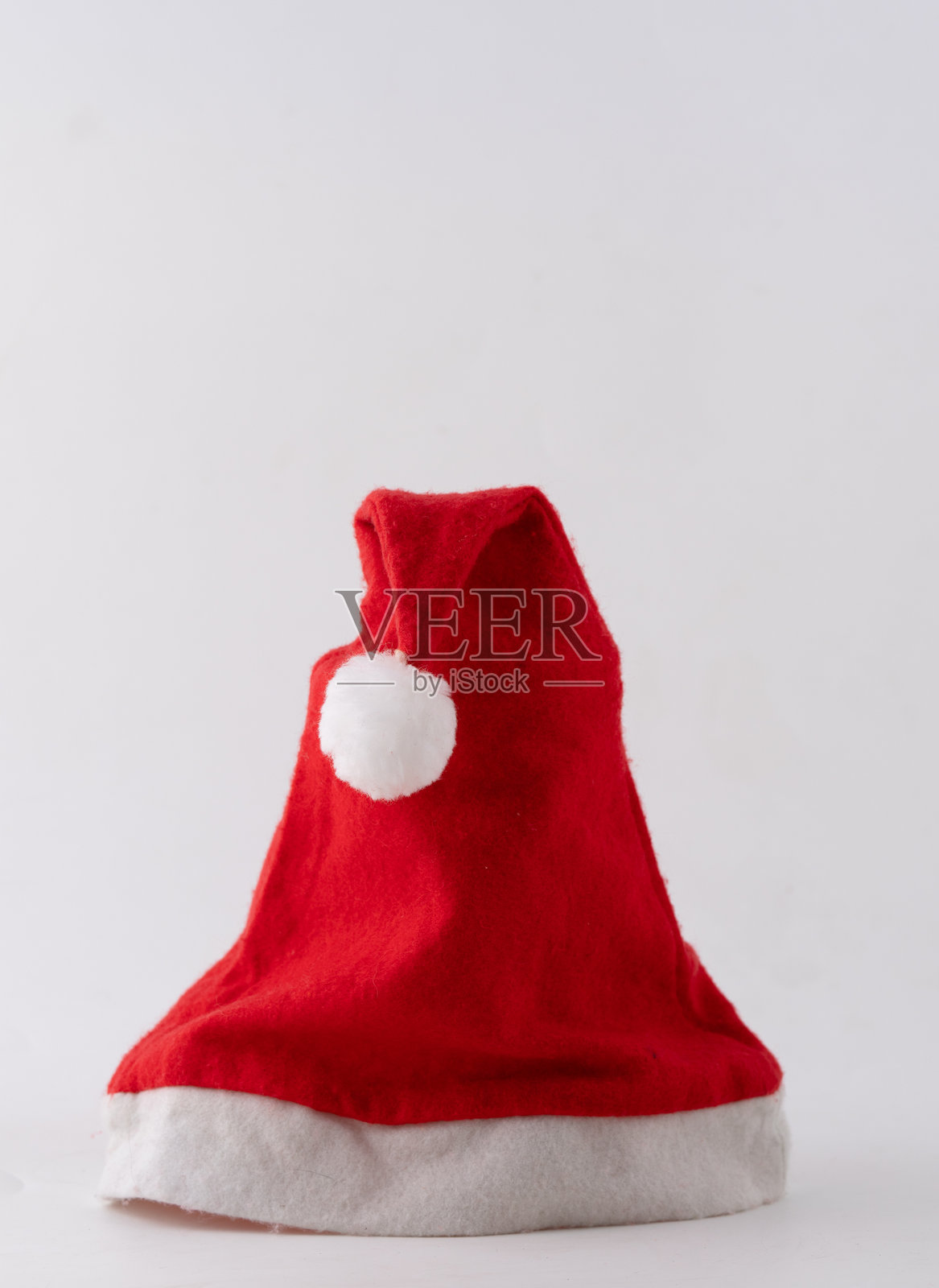 一顶鲜红色的圣诞老人帽，顶部装饰着蓬松的白色球球照片摄影图片