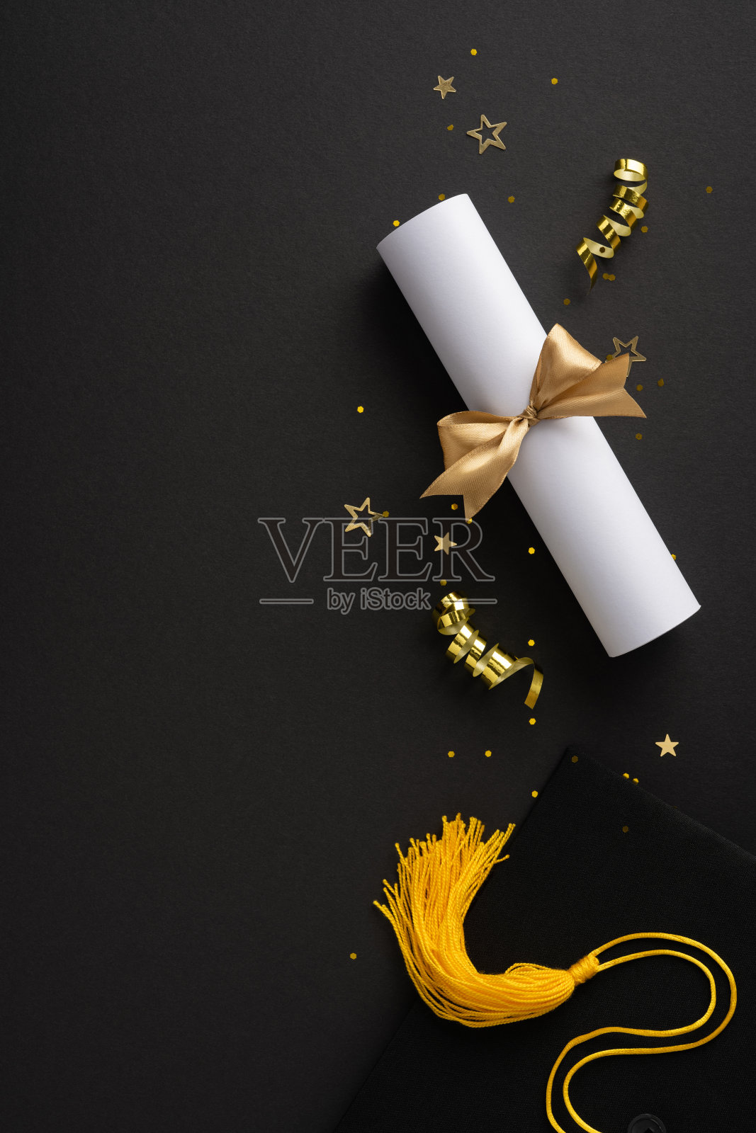 象征毕业的垂直物品，包括绑有金色丝带的文凭卷轴，放置在深色表面上照片摄影图片