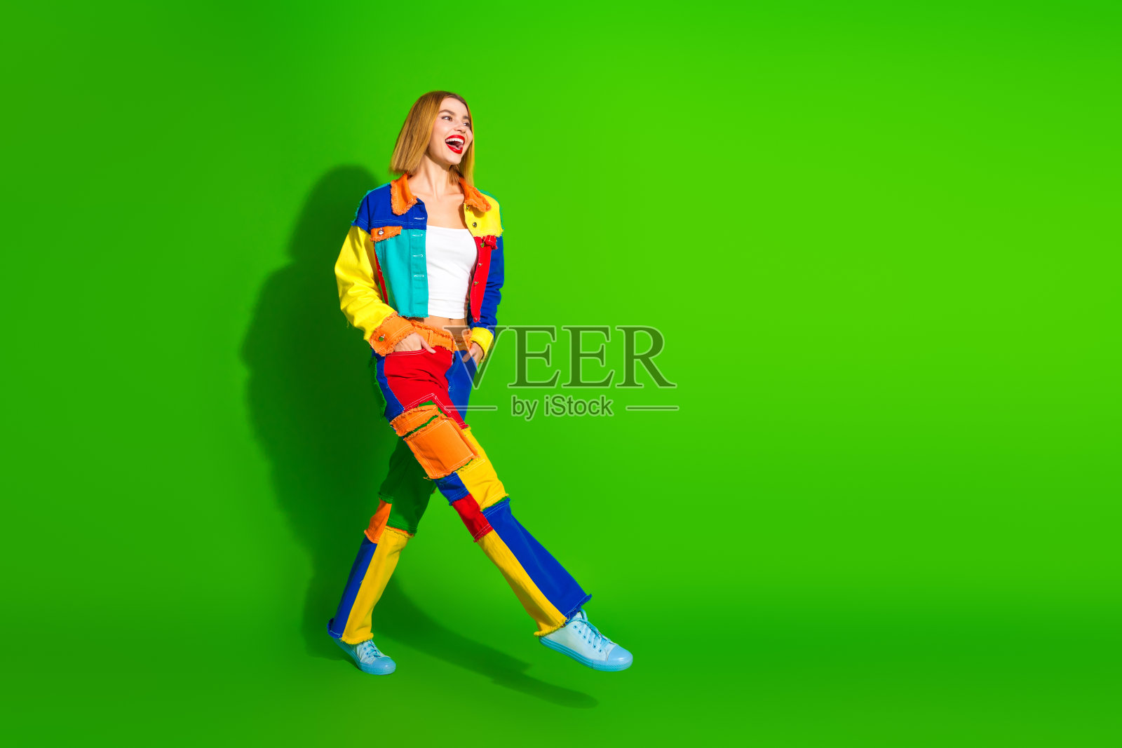 年轻女性穿着色彩斑斓的服装，自信地走在绿色背景上，展现时尚、风格、自信和充满活力的生活方式。照片摄影图片