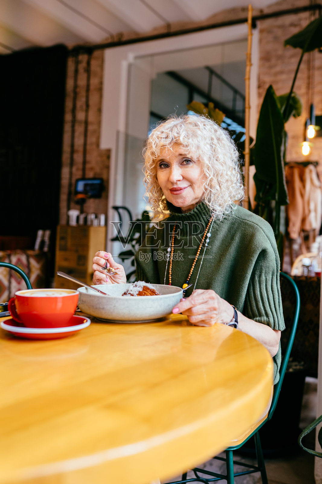 蓝眼睛和卷曲金发的老年女性特写肖像，正在喝咖啡。直接的眼神交流，时尚的妆容，自然的表情。优雅衰老的概念。照片摄影图片