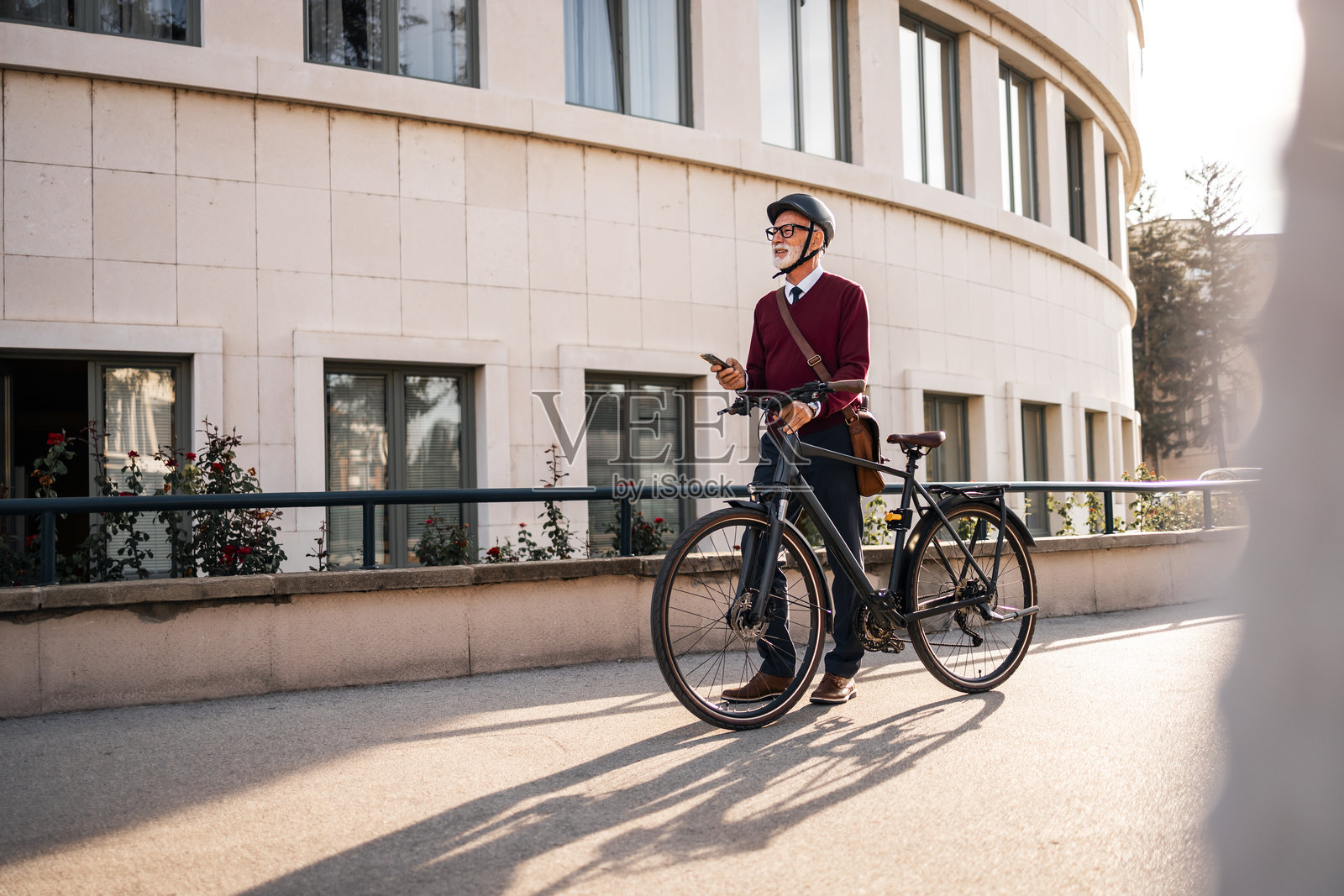 老年男子在城市办公楼附近骑自行车通勤照片摄影图片
