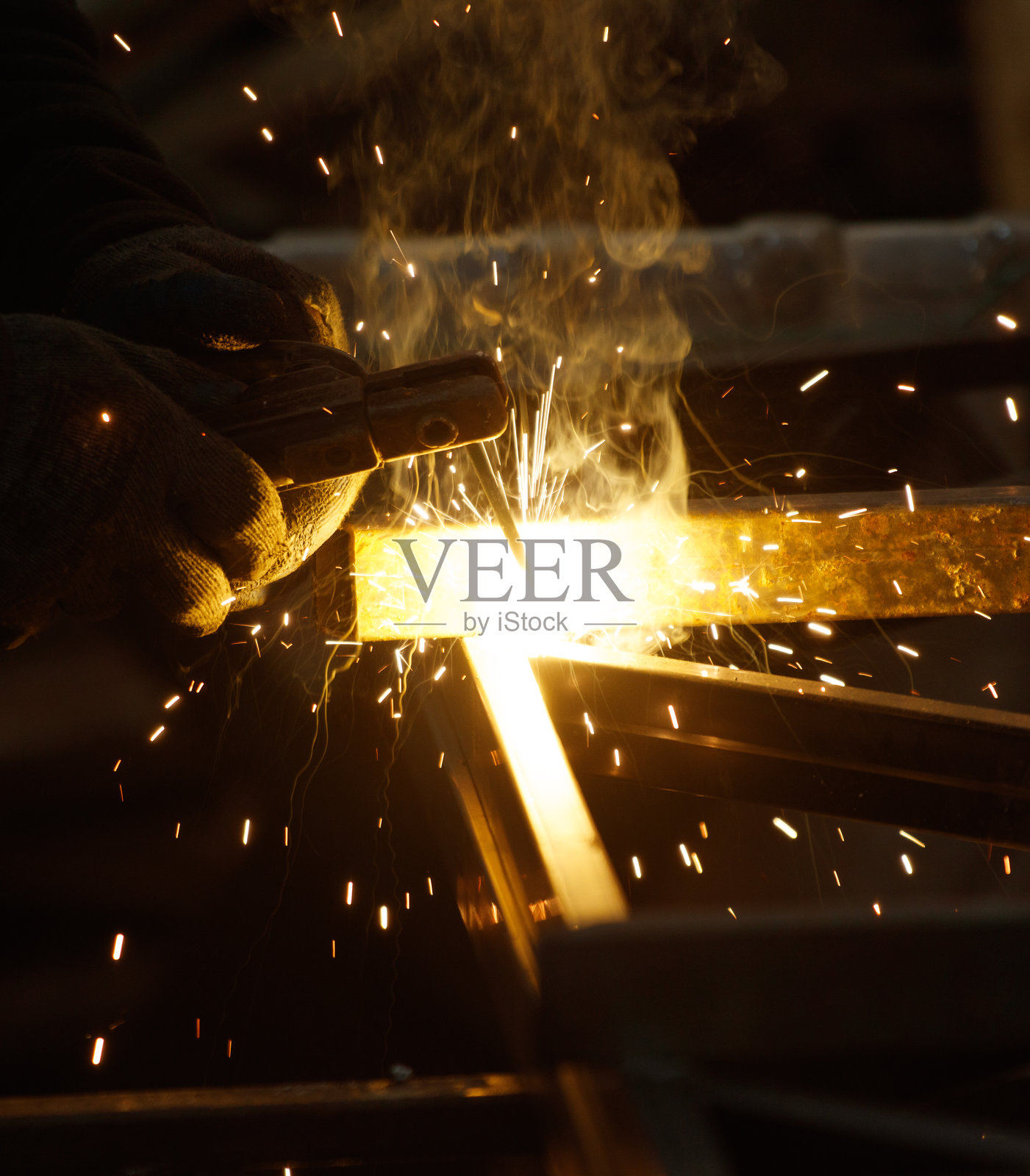 一个男人正在焊接一块金属，产生火花和烟雾。照片摄影图片