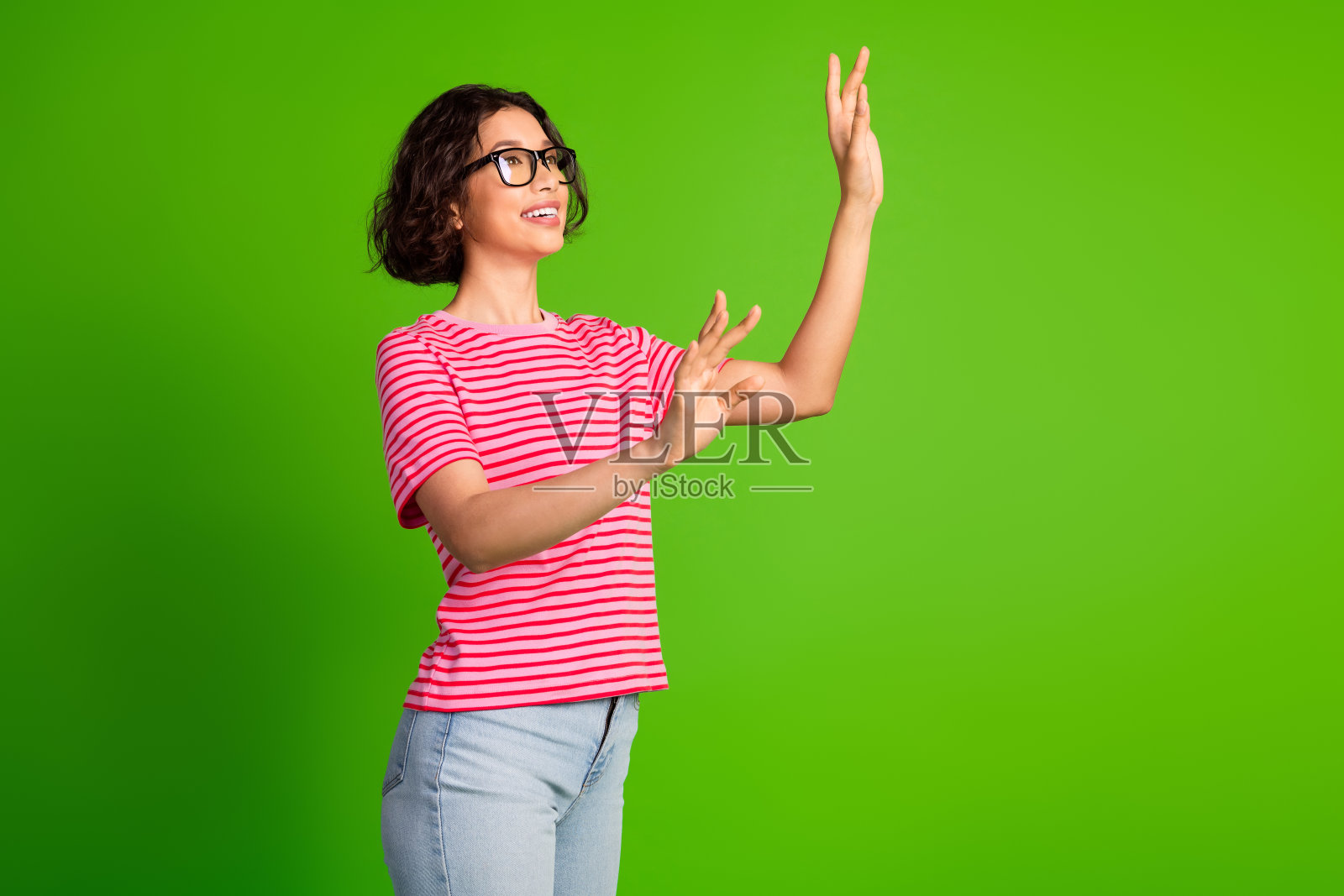 年轻美丽的女性穿着条纹衬衫，自信地摆姿势，手势表现出活力，背景为鲜艳的绿色。照片摄影图片