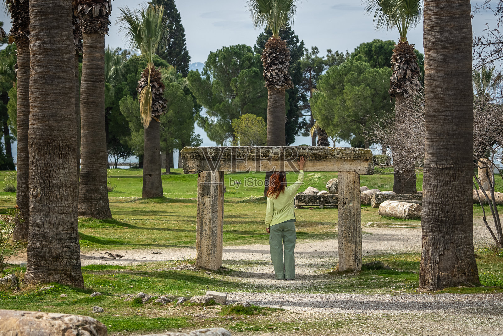 一位成熟的女性在阳光明媚的日子里，享受着古老遗址和树木之间宁静的氛围。照片摄影图片