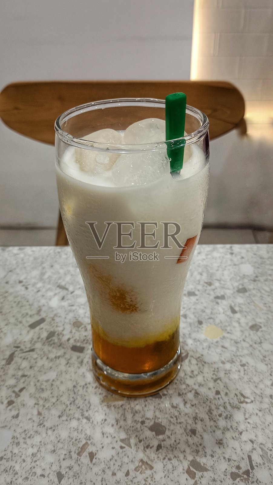 一杯分层饮料，底部是橙色糖浆，上面是奶油白色泡沫。盛在高脚杯中，配有绿色吸管和果冻块，看起来丰富、甜美且令人沉醉。照片摄影图片
