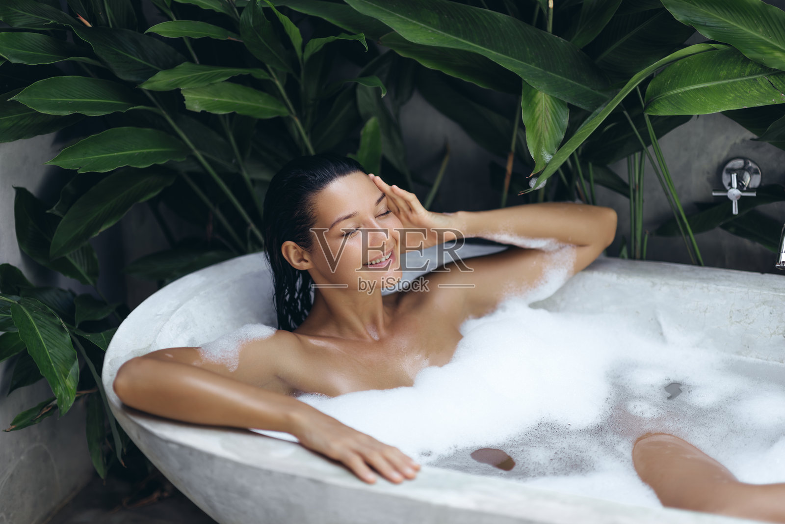 放松的女性在户外热带浴缸中享受泡泡浴照片摄影图片