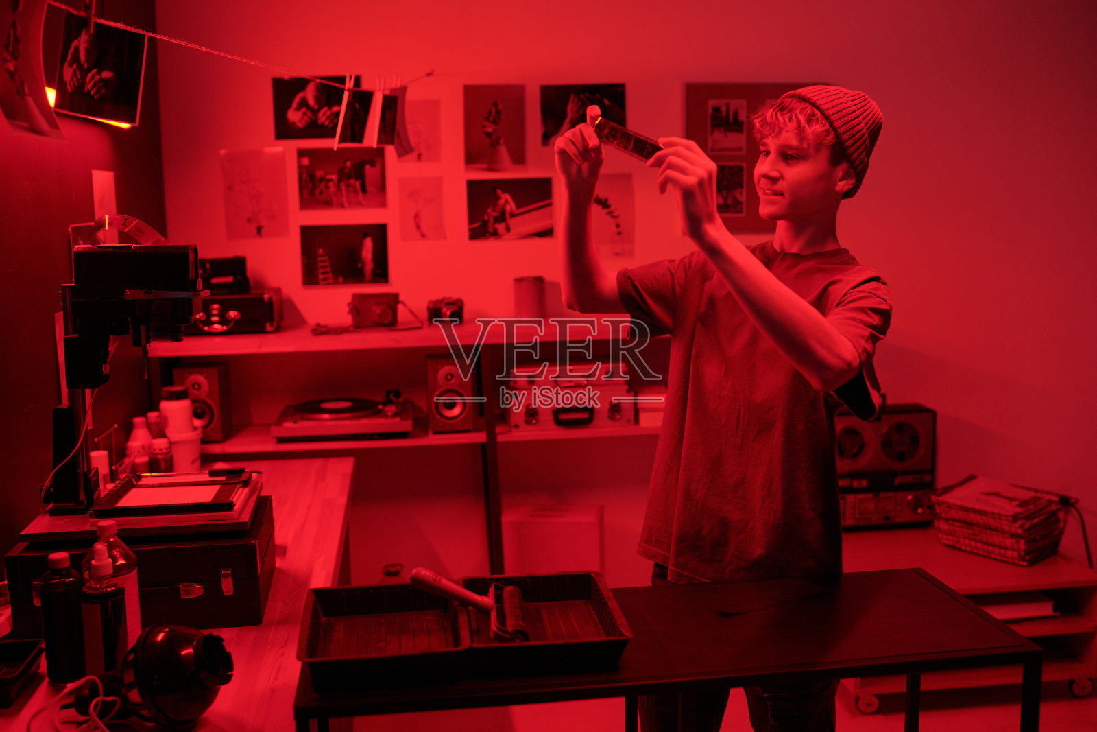 微笑的少年在暗房中红光下查看底片，回顾胶卷。照片摄影图片