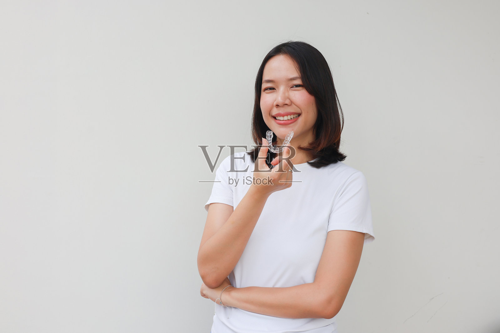 特写年轻可爱的亚洲女性手持牙齿矫正器，背景为白色，适用于美齿内容和牙科治疗课程概念。照片摄影图片