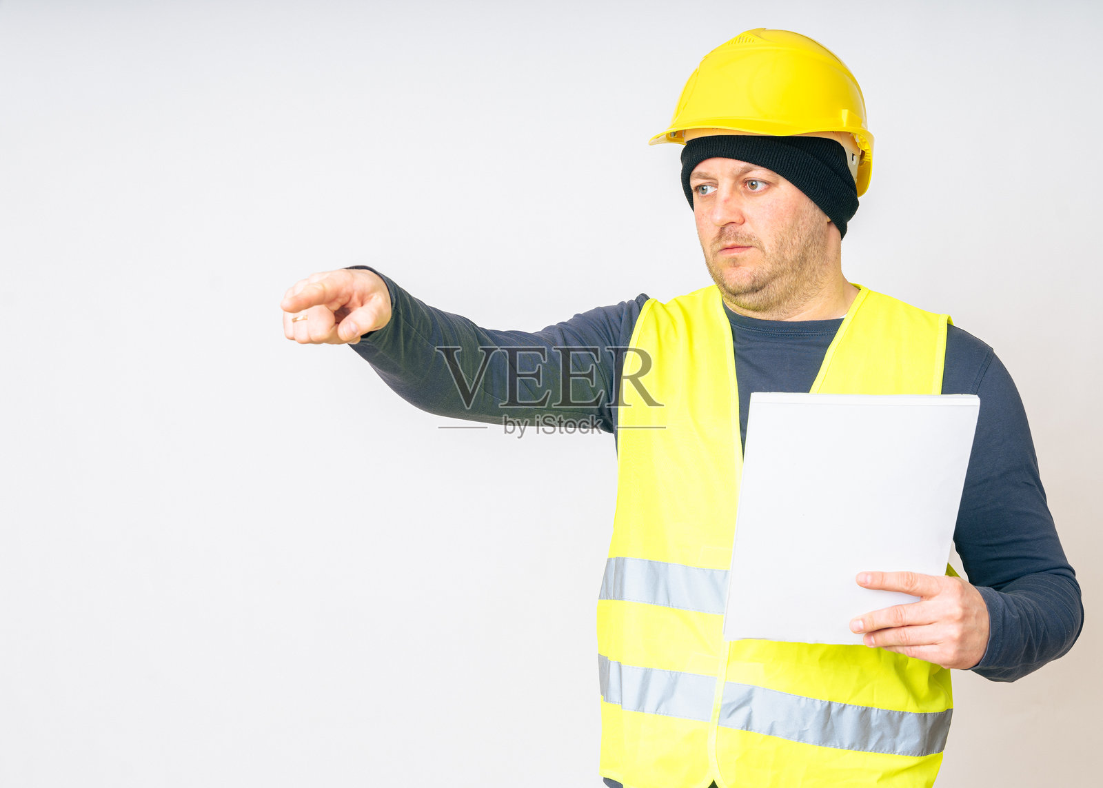 一名穿着黄色工作背心、工装和黄色安全头盔，手中拿着文件的男子照片摄影图片