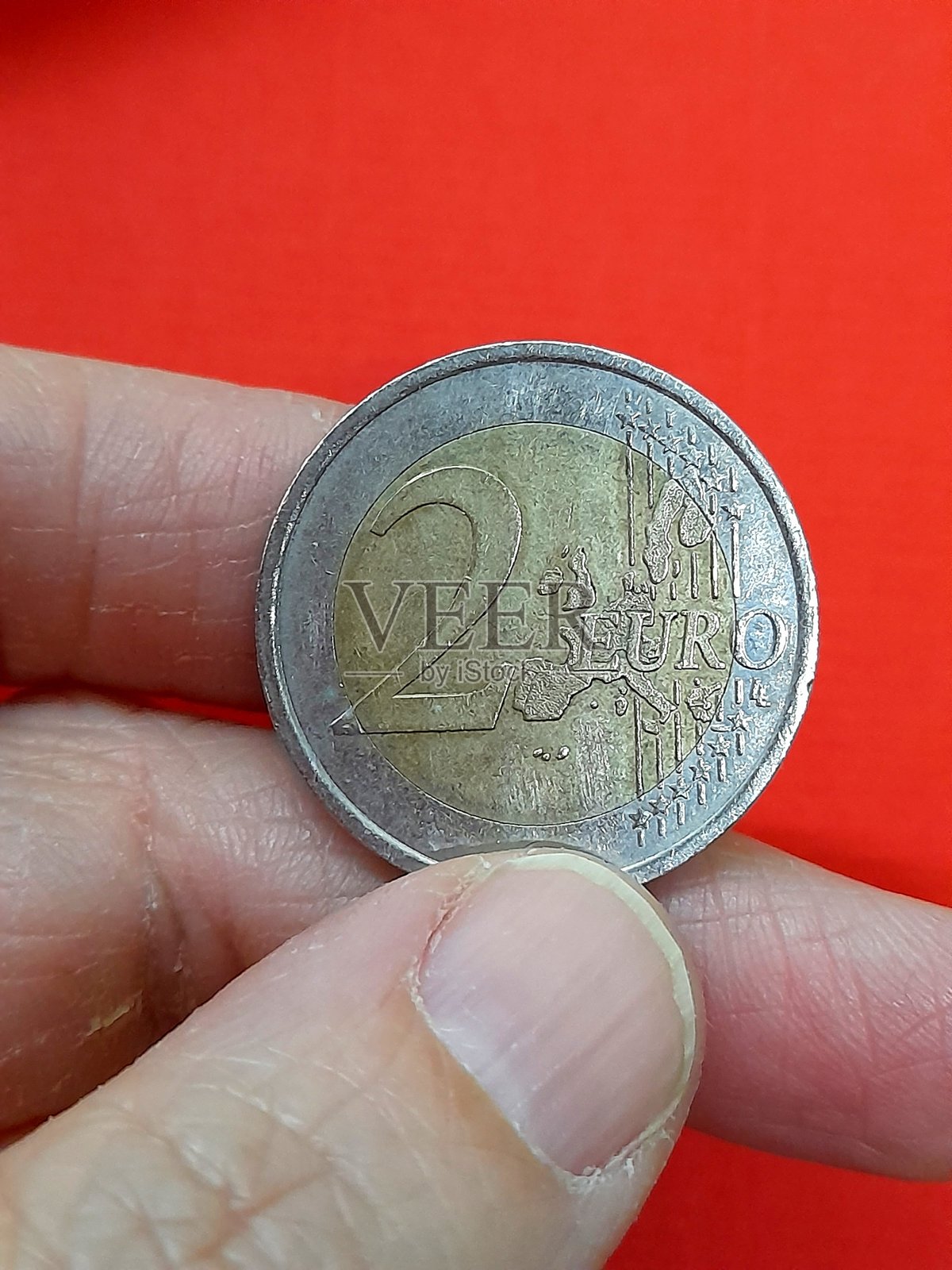 手中握着的2欧元硬币，背景为红色照片摄影图片