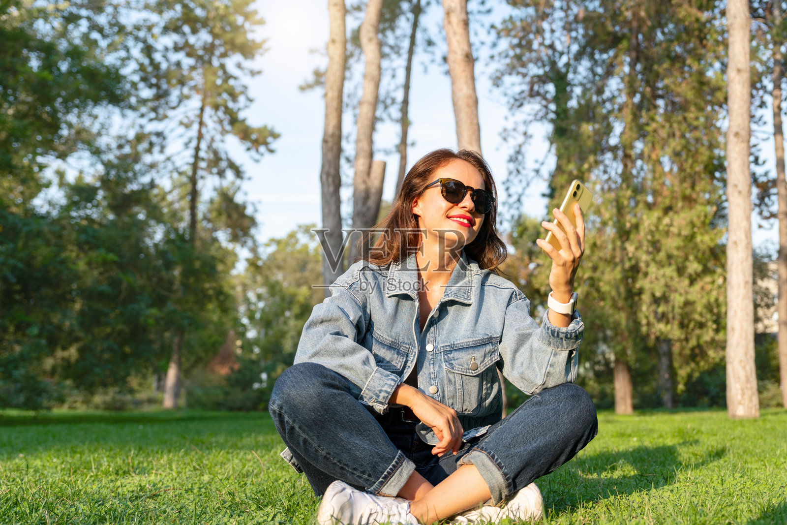 微笑的城市女性穿着休闲服装，坐在公园的草地上用智能手机发信息照片摄影图片