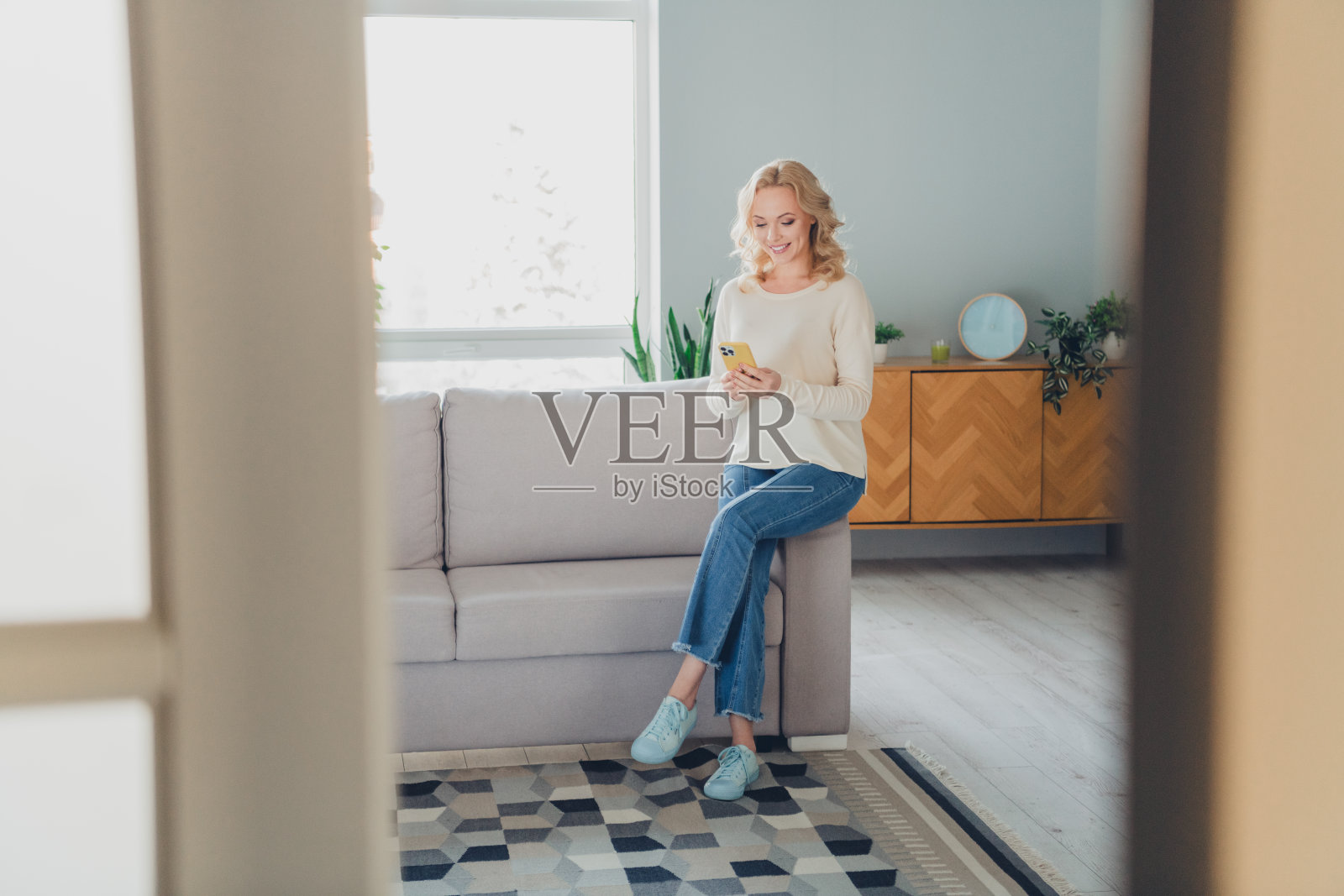 明亮舒适的客厅，一位愉快的女性在时尚舒适的家居环境中享受闲暇时光，使用她的智能手机。照片摄影图片