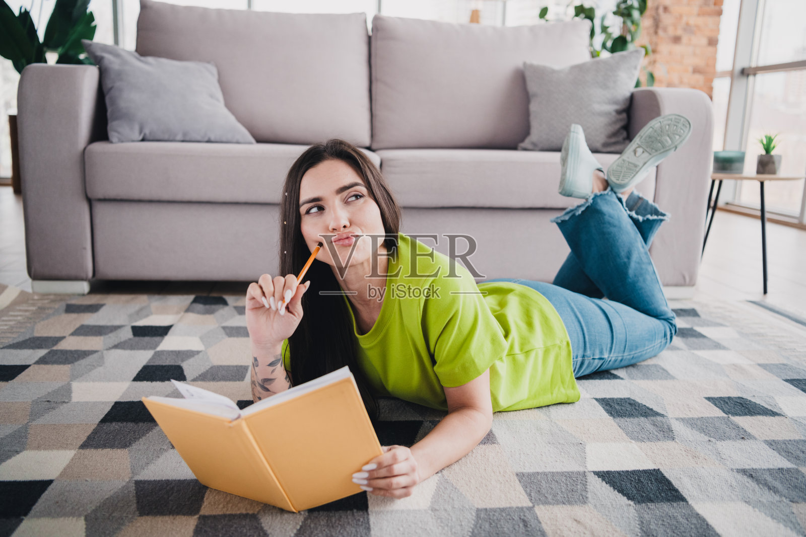 年轻女性躺在现代舒适的客厅地板上，手里拿着一本书，享受闲暇时光照片摄影图片