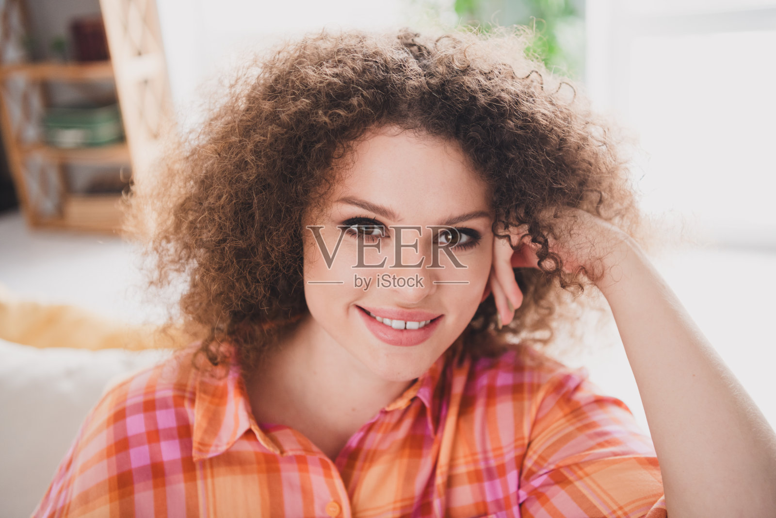 微笑的年轻女性，留着自然卷发，穿着休闲的格子衬衫，在明亮的阳光下享受舒适的家庭时光。照片摄影图片