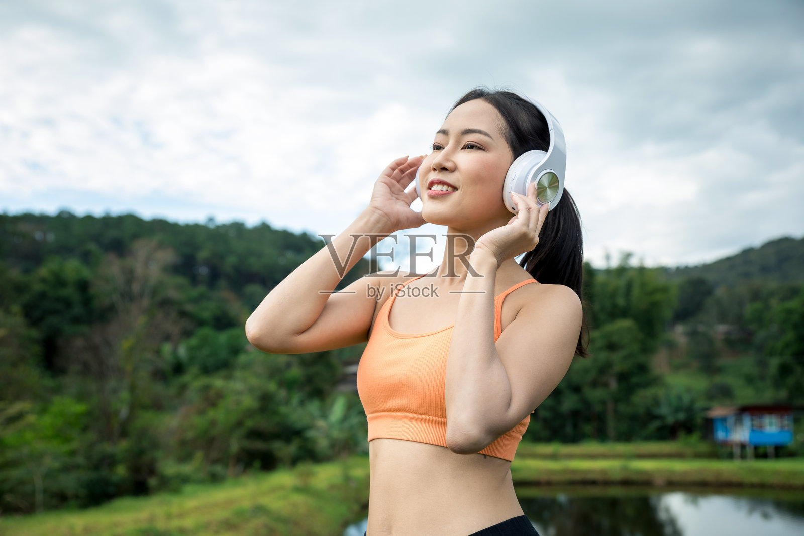 年轻亚洲女性特写肖像，戴着耳机，享受疗愈音乐和阳光，户外。女性瑜伽练习者佩戴无线耳机，背景是森林。照片摄影图片