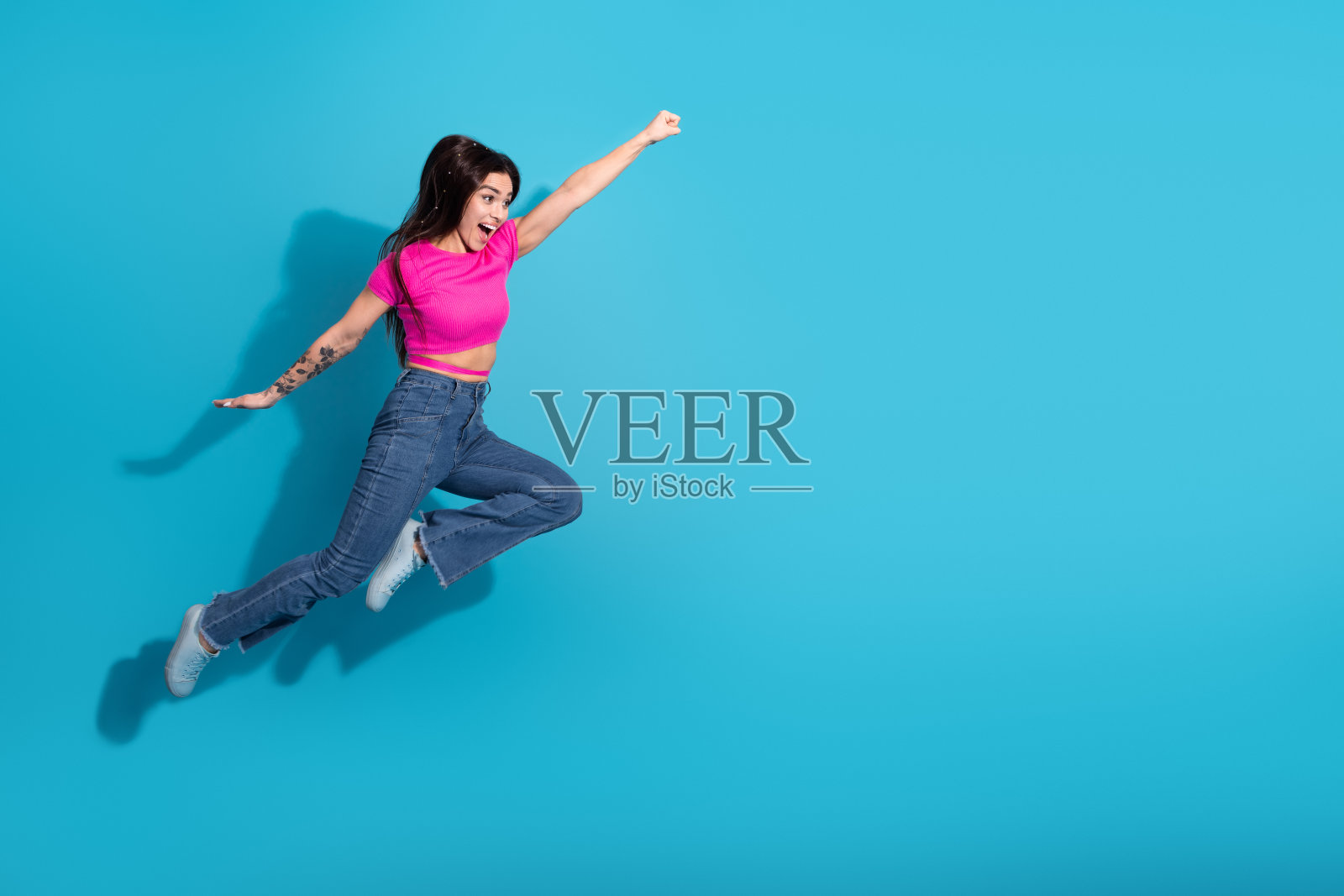 充满活力的年轻女性穿着休闲时尚的服装，在纯蓝色背景下欢快地跳跃，展现出动感的姿态照片摄影图片