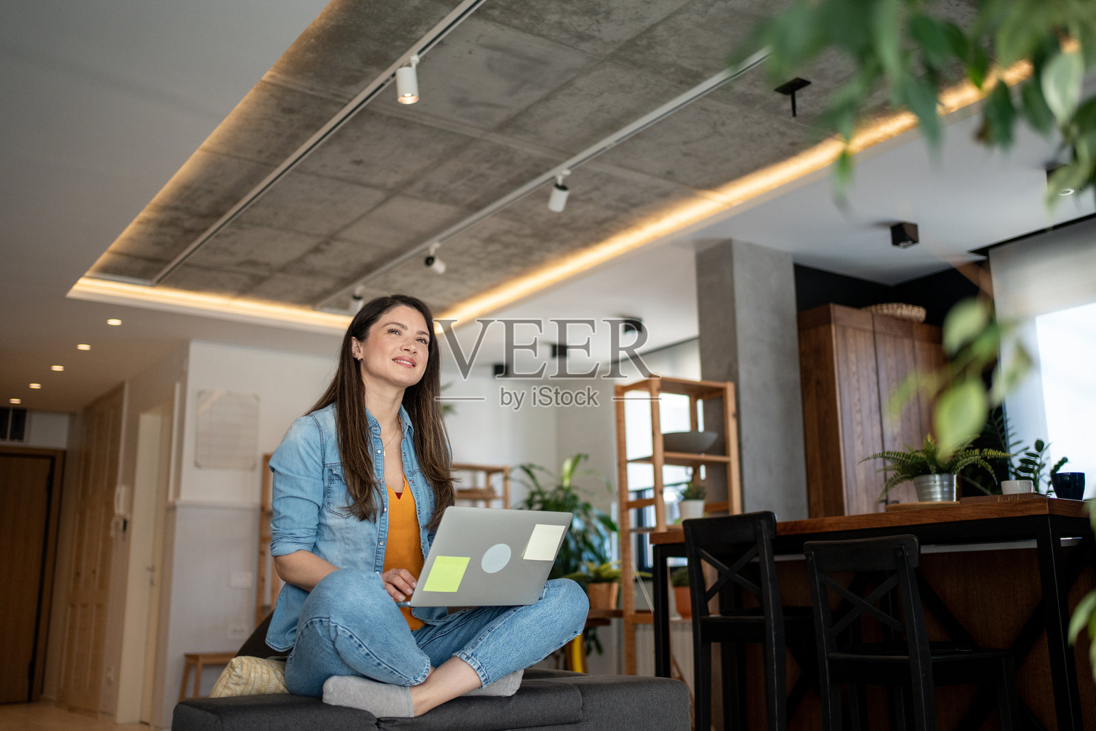 在家工作的女性坐在沙发上使用笔记本电脑，目光投向远方，陷入沉思。照片摄影图片