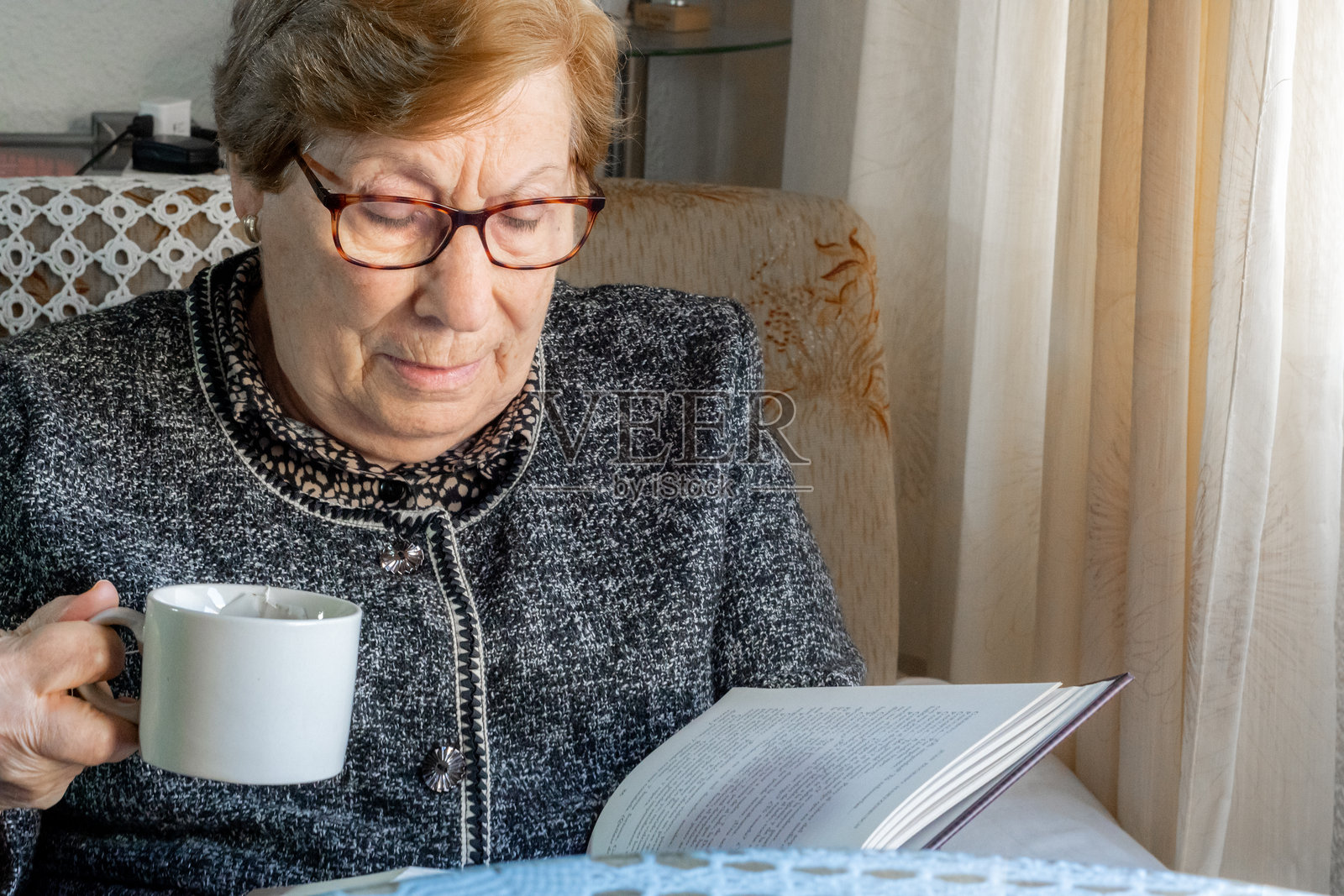 一位老年女性在家中窗边阅读一本书照片摄影图片