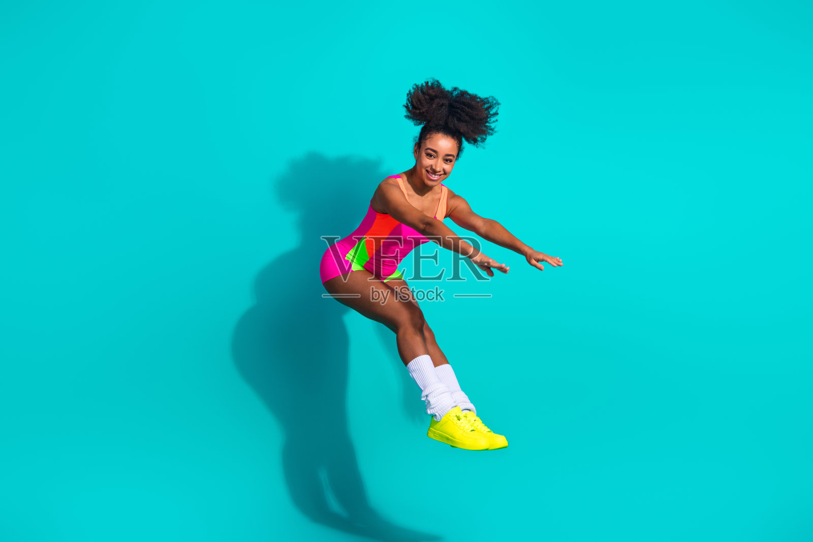 年轻的运动女性穿着色彩鲜艳的运动服，在青绿色背景下充满活力地跳跃照片摄影图片