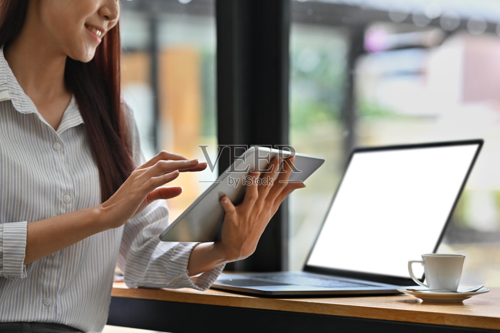 一位年轻的职业女性在桌子上使用数字平板电脑，旁边有一台笔记本电脑和咖啡杯，利用科技提高现代工作空间的效率。照片摄影图片