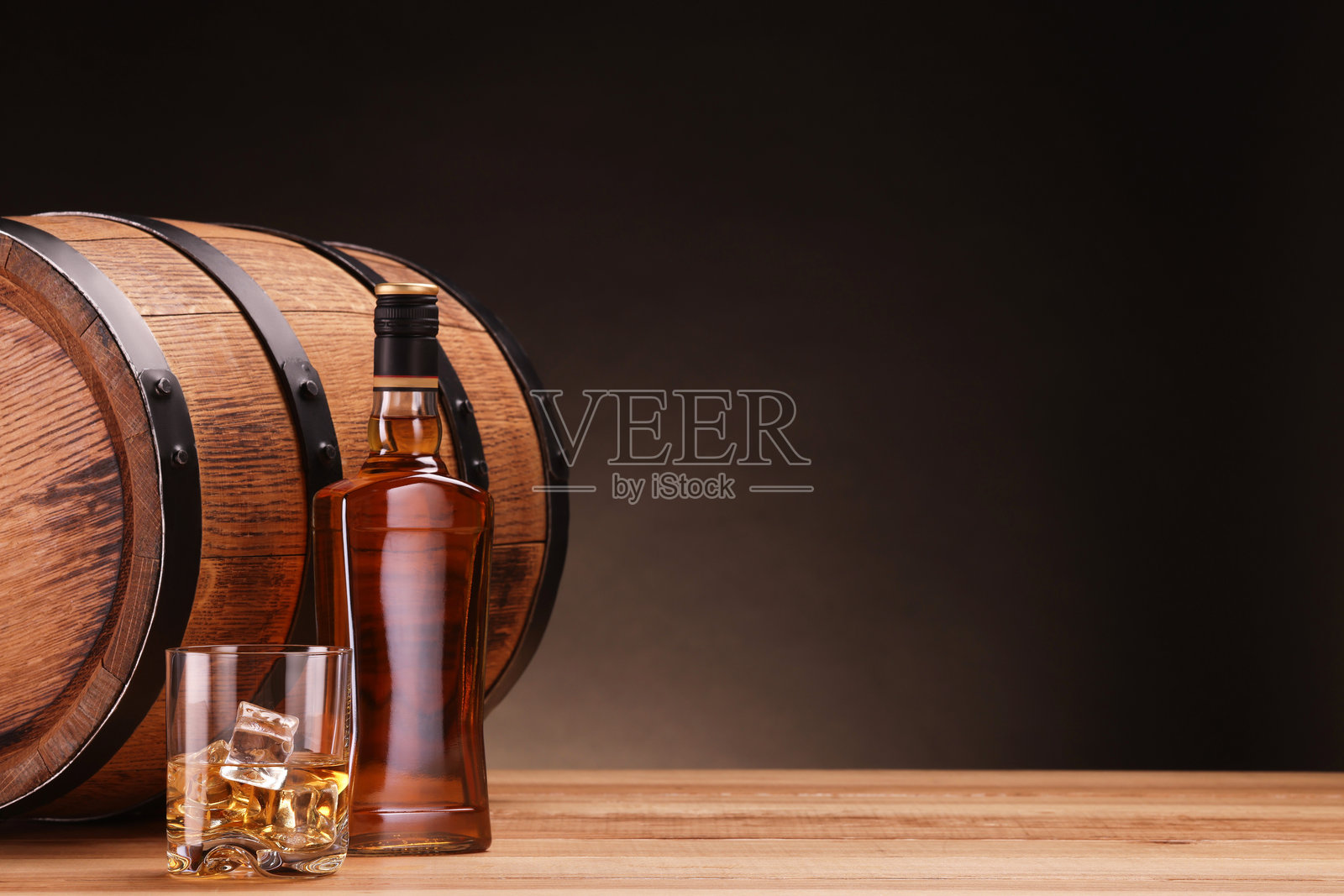玻璃杯中装有冰块的威士忌，旁边有瓶子和木桶，背景为深色，留有文字空间照片摄影图片