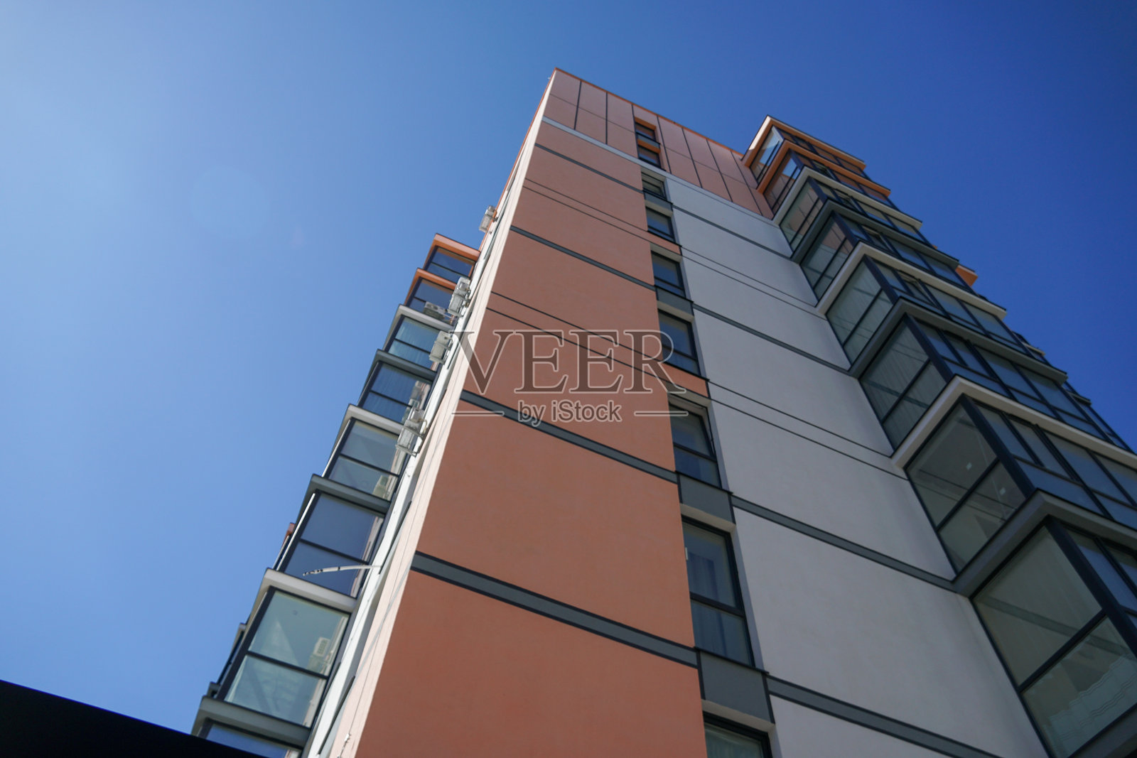 一座高耸的现代住宅建筑在晴朗的蓝天下显得格外醒目，展示出其鲜艳的色彩和现代建筑风格。照片摄影图片