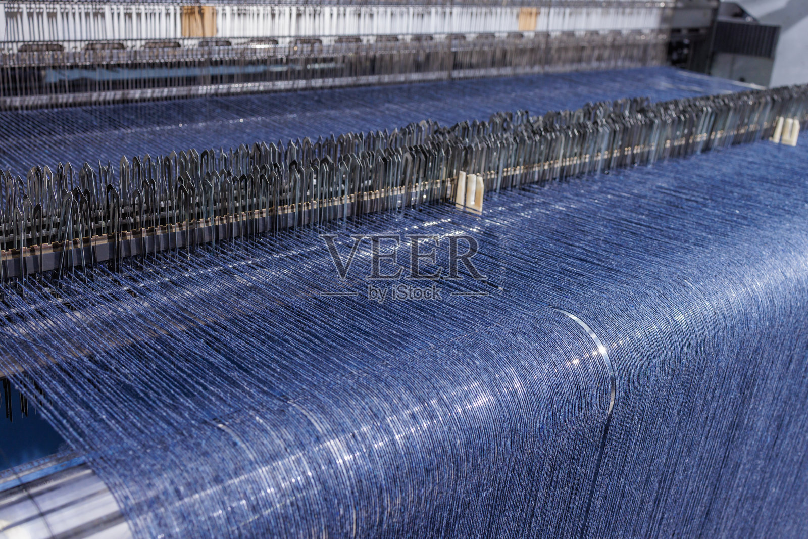 现代纺织制造厂中，工业织机上蓝色线材正在编织面料。照片摄影图片