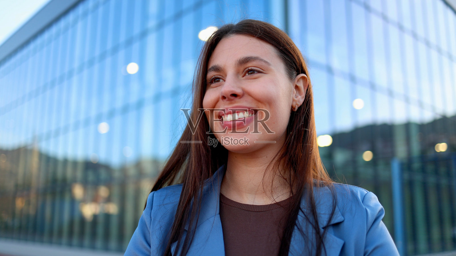 年轻的女商人微笑着望向办公室大楼旁边。照片摄影图片