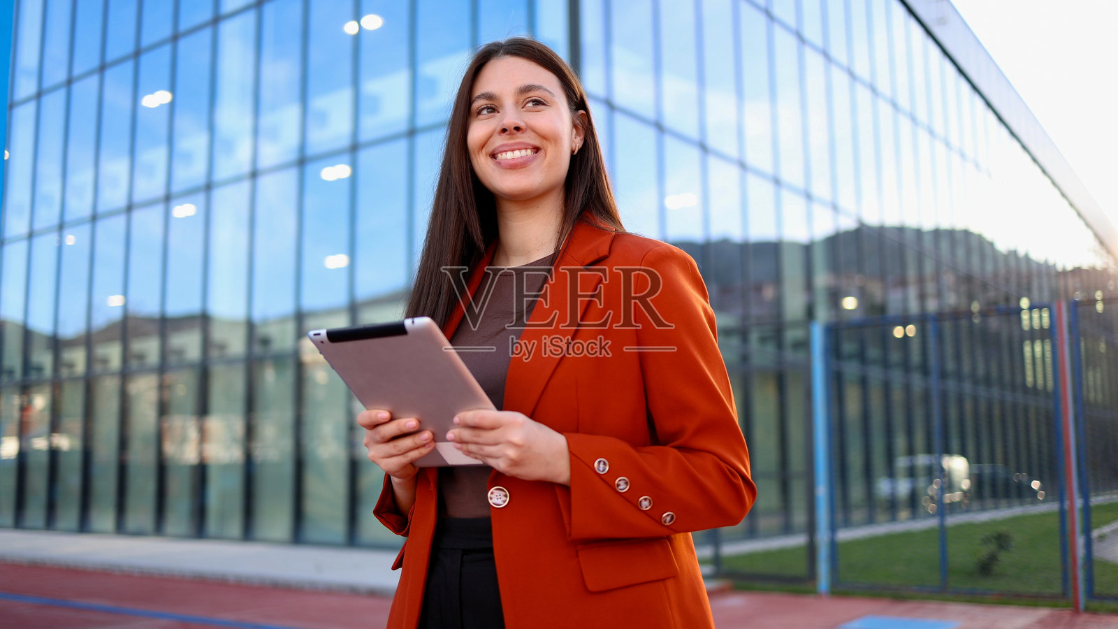 微笑的女商人手持平板，望向现代办公大楼。照片摄影图片