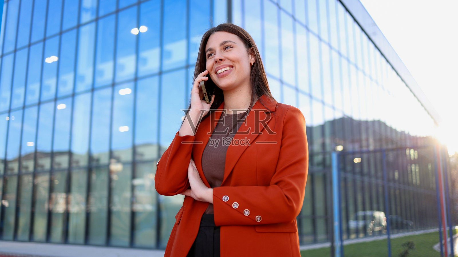 在办公大楼前微笑的女商人正在打电话照片摄影图片