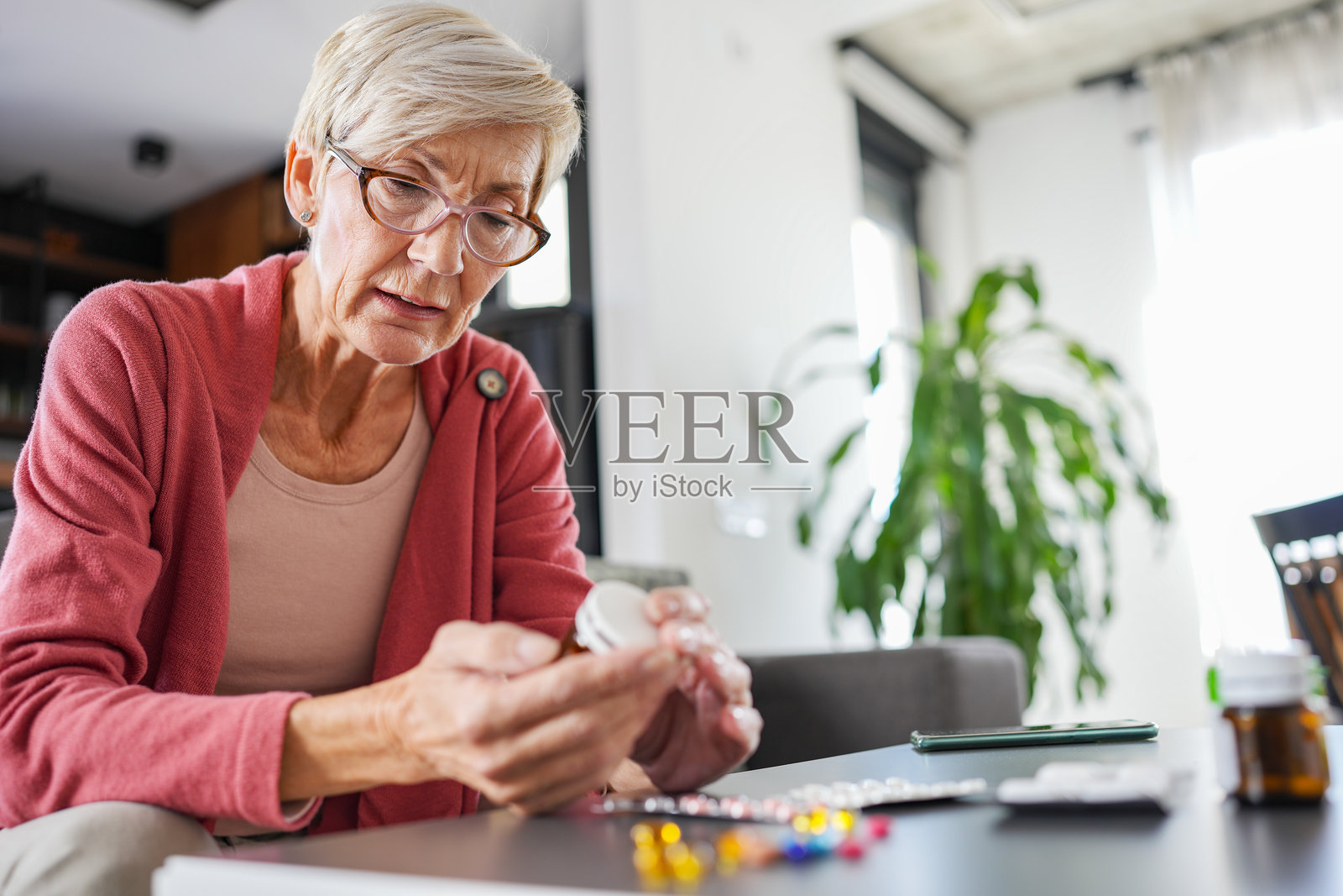 一位年长女性在家中仔细阅读处方瓶。她负责任地管理自己的药物，确保获得适当的医疗保健和治疗，以维持健康的生活方式。照片摄影图片