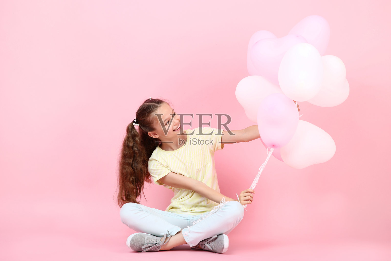 可爱的小女孩坐在粉色背景上，手里拿着气球。照片摄影图片