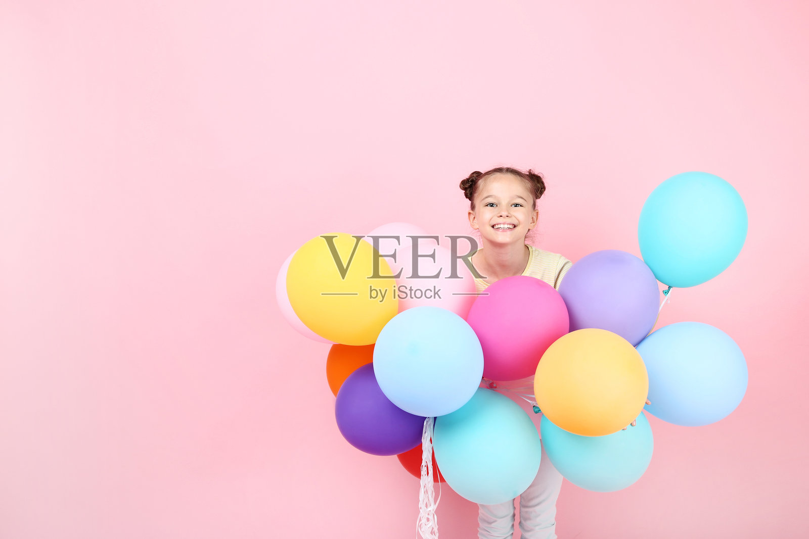 可爱的小女孩手持彩色气球，背景为粉色照片摄影图片
