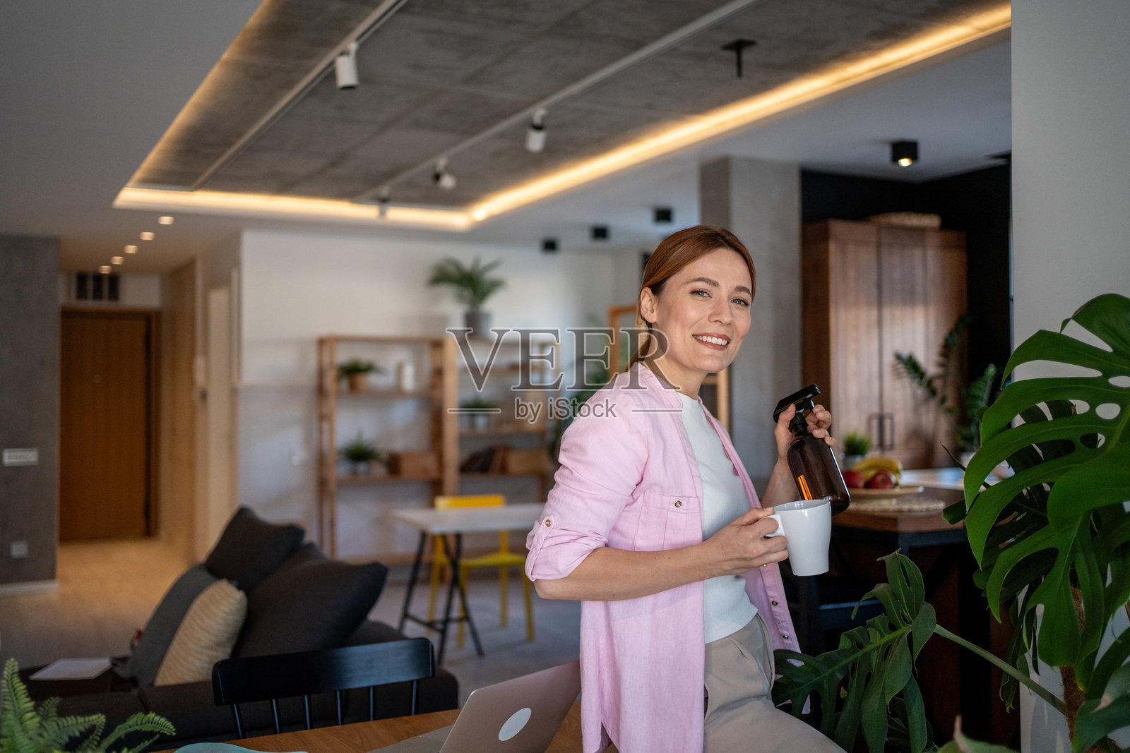 女人在现代公寓里照顾植物，同时喝咖啡照片摄影图片