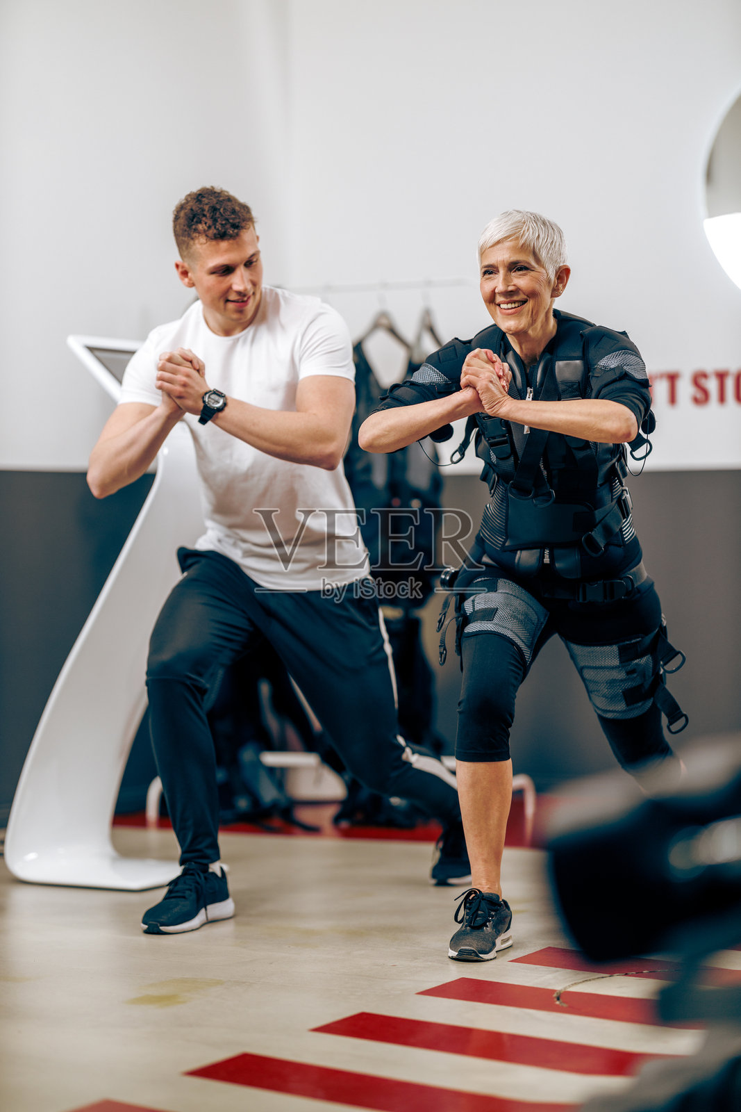 老年女性在健身房与教练一起进行EMS锻炼照片摄影图片