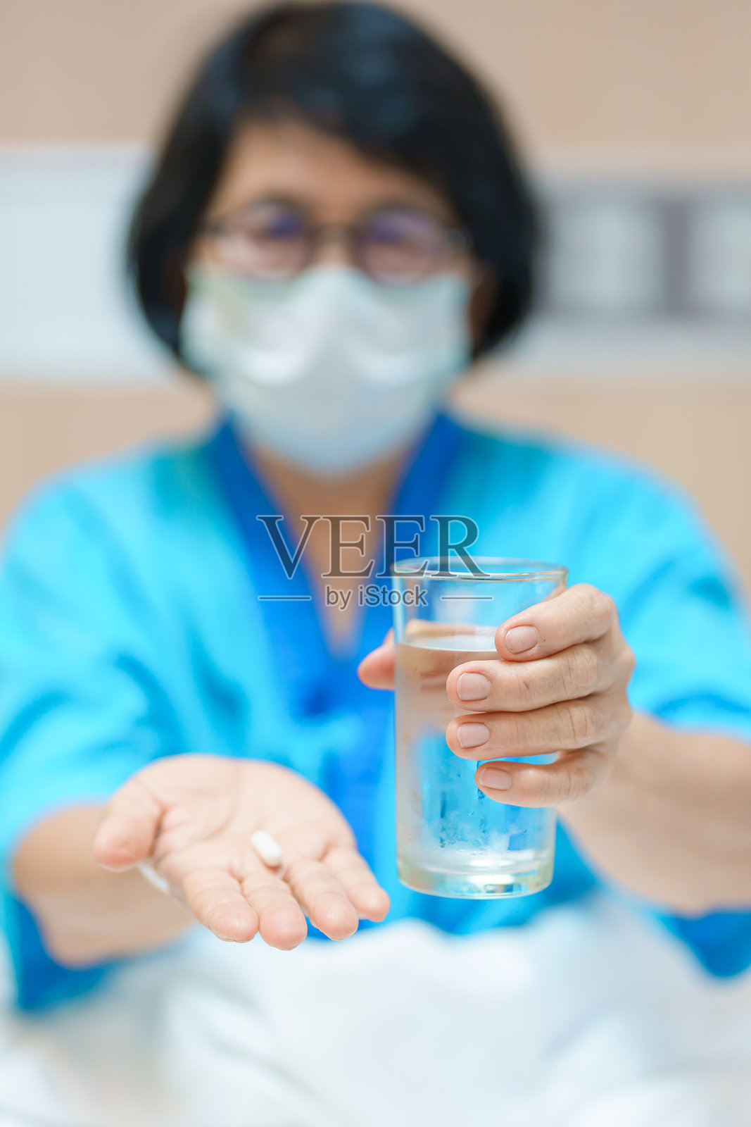 老年亚洲女性患者手握药丸和一杯清水。女性老年人在医院服用药片。流感、发烧、疾病、治疗、保险、医疗和用药日。照片摄影图片